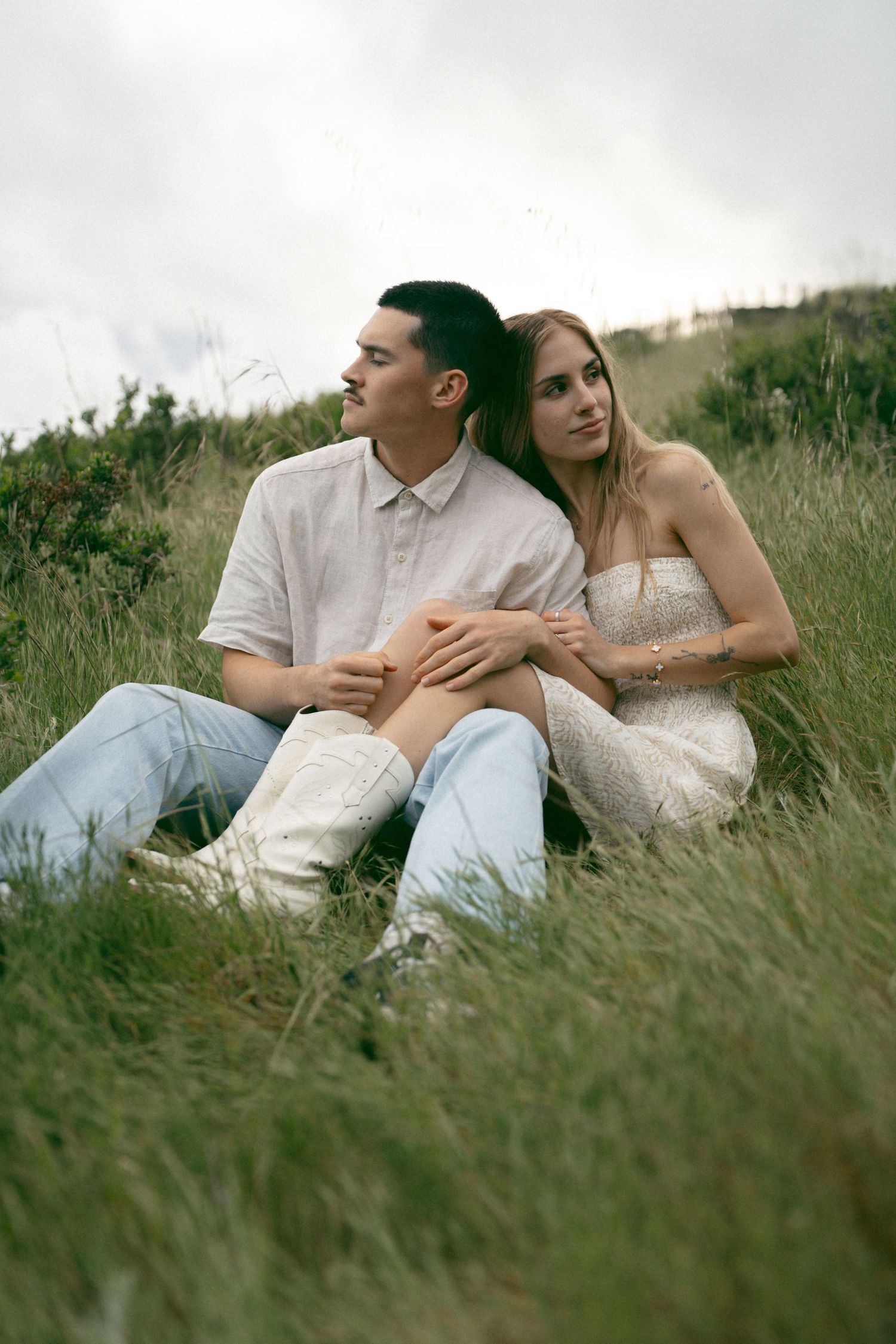 Romantic couple lying together in tall grass during an outdoor photo session.