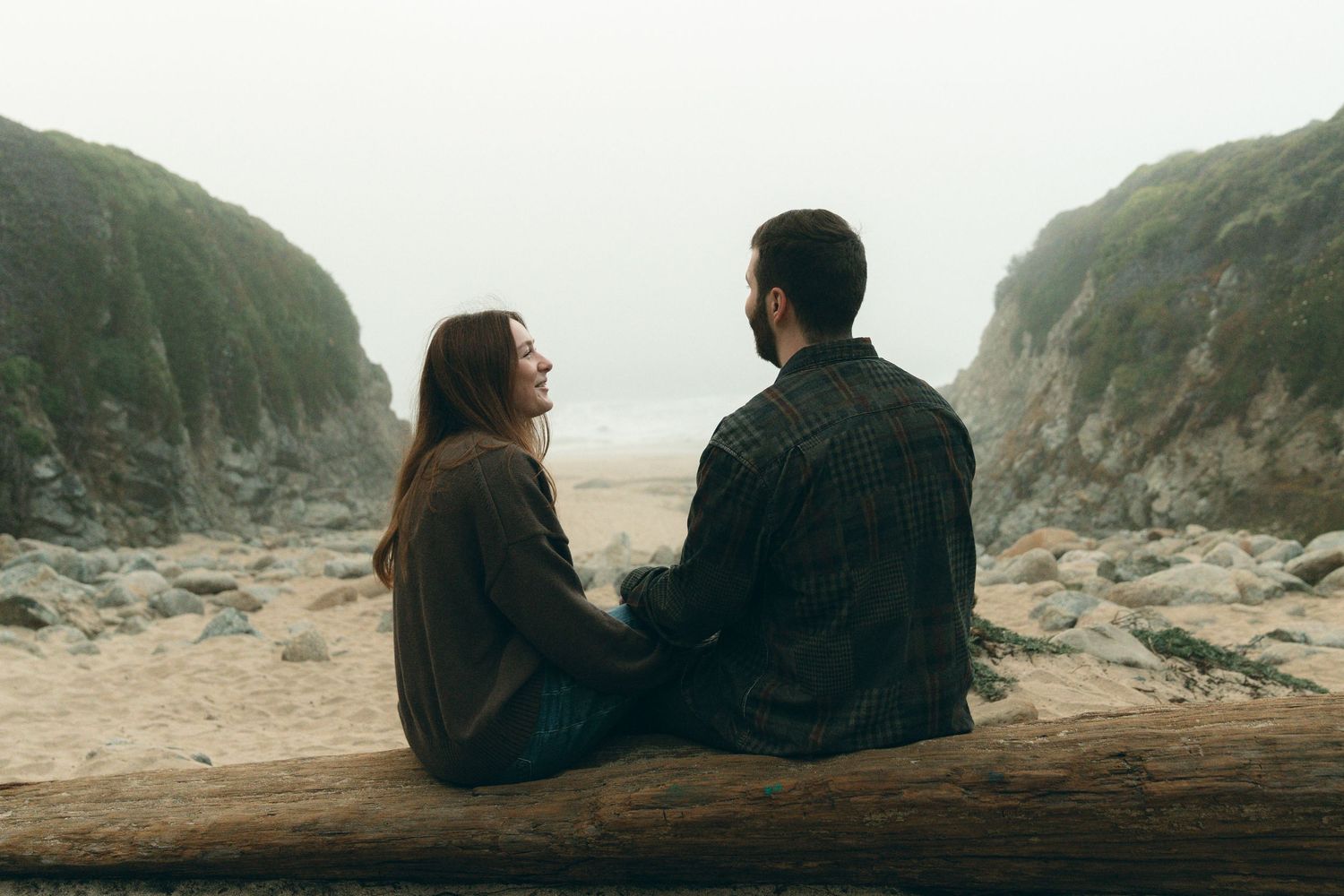 A couple sits together overlooking dramatic coastal cliffs and crashing waves at sunset.