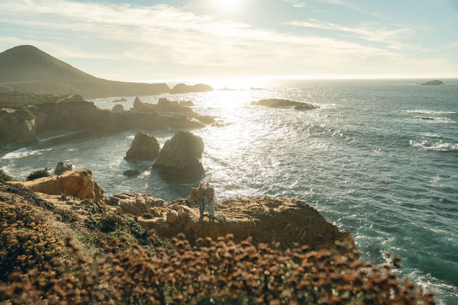Dramatic oceanfront vista with rugged coastline and sunlit waves breaking against rocky outcrops.