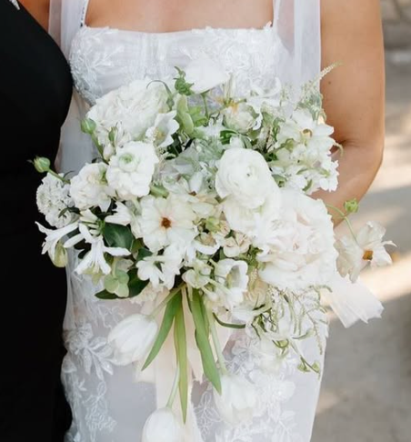 Close-up of an elegant white bridal bouquet featuring roses and mixed florals with soft green accents.