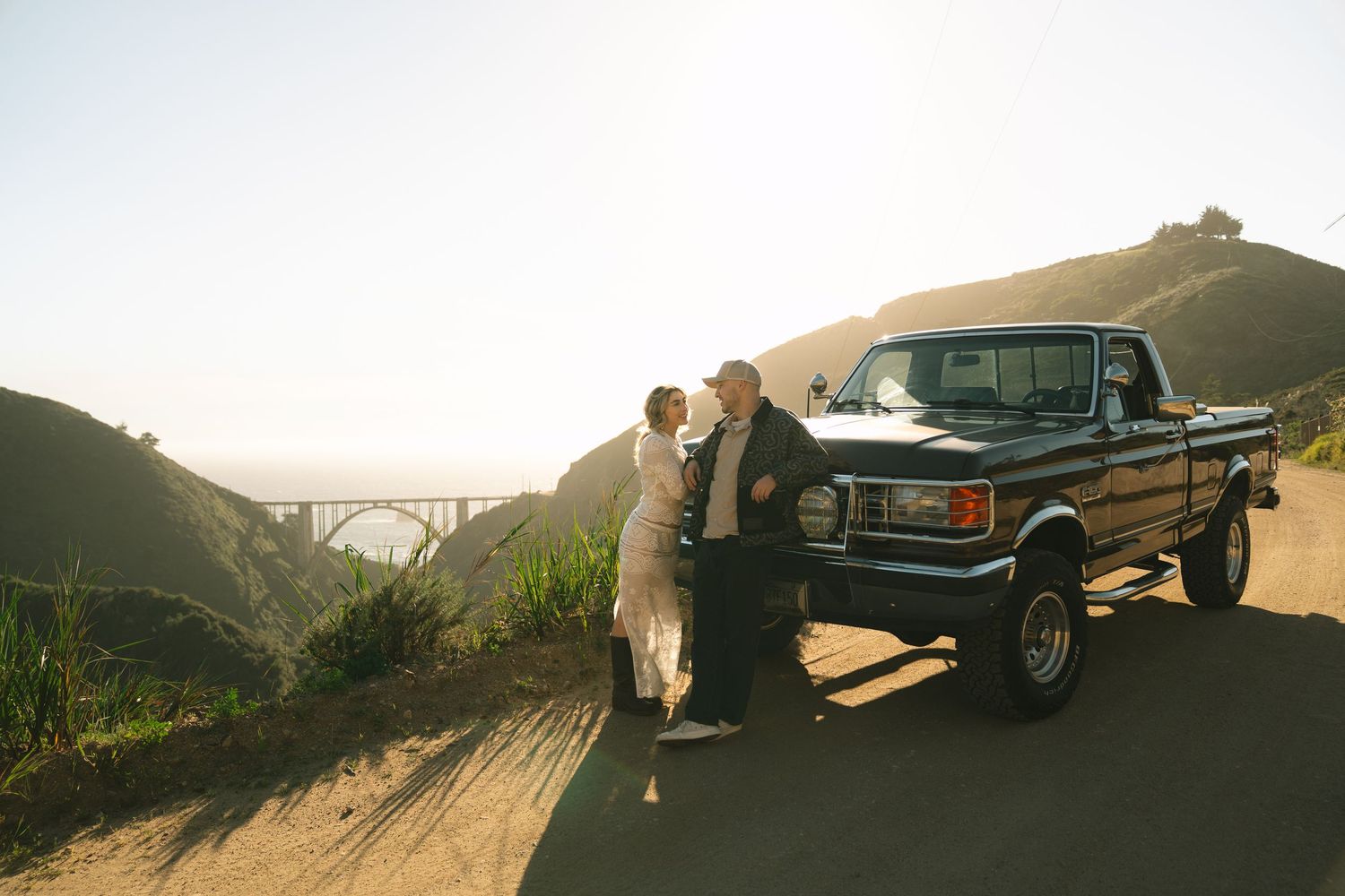 Vintage Mercedes-Benz car parked on a scenic mountain road at sunset with golden light illuminating the landscape.