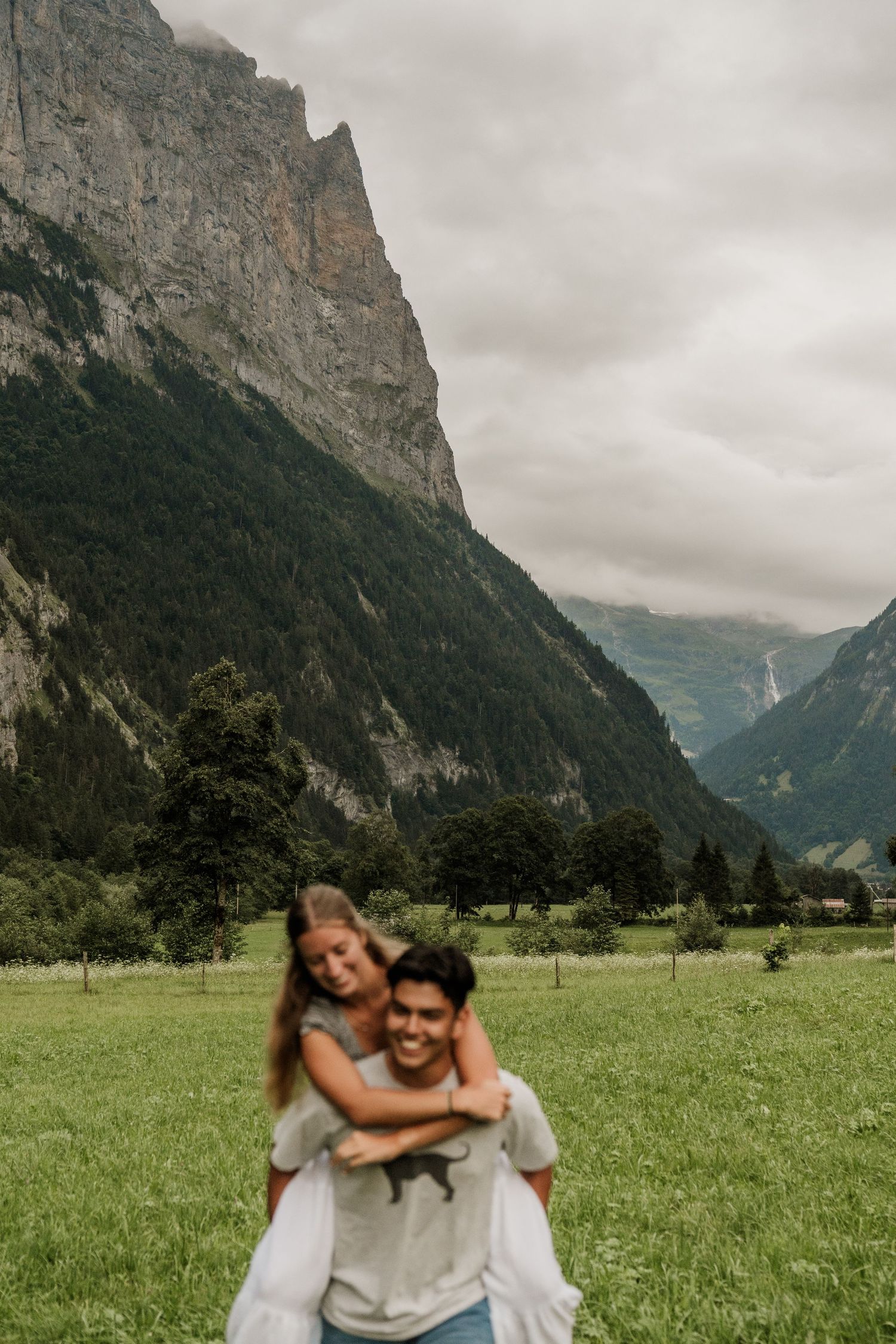 A scenic mountain valley in Switzerland with dramatic cliffs and green meadows on a cloudy day.
