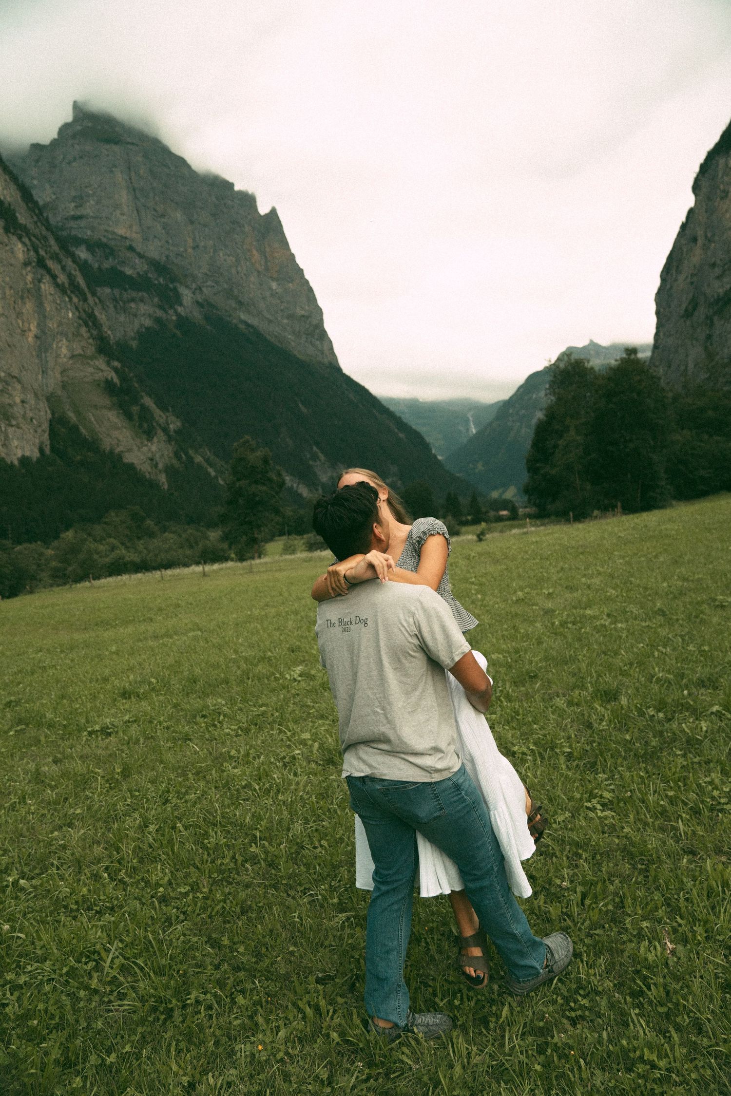 A couple embracing in a dramatic alpine meadow with mountain peaks in the background.