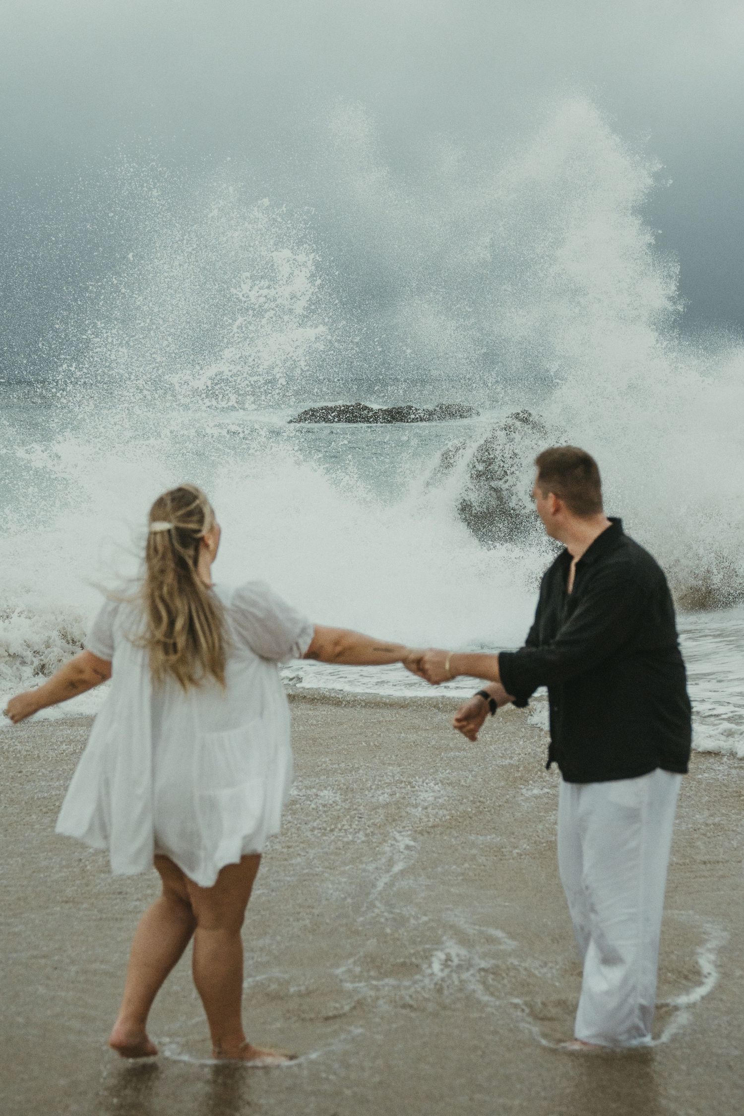 A sequence of photos shows a couple getting splashed by dramatic ocean waves along a rocky shoreline.