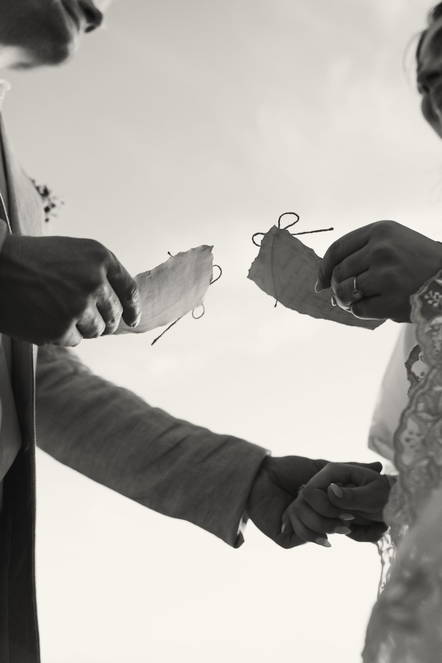 Black and white photo of bride and groom exchanging wedding rings during outdoor ceremony.