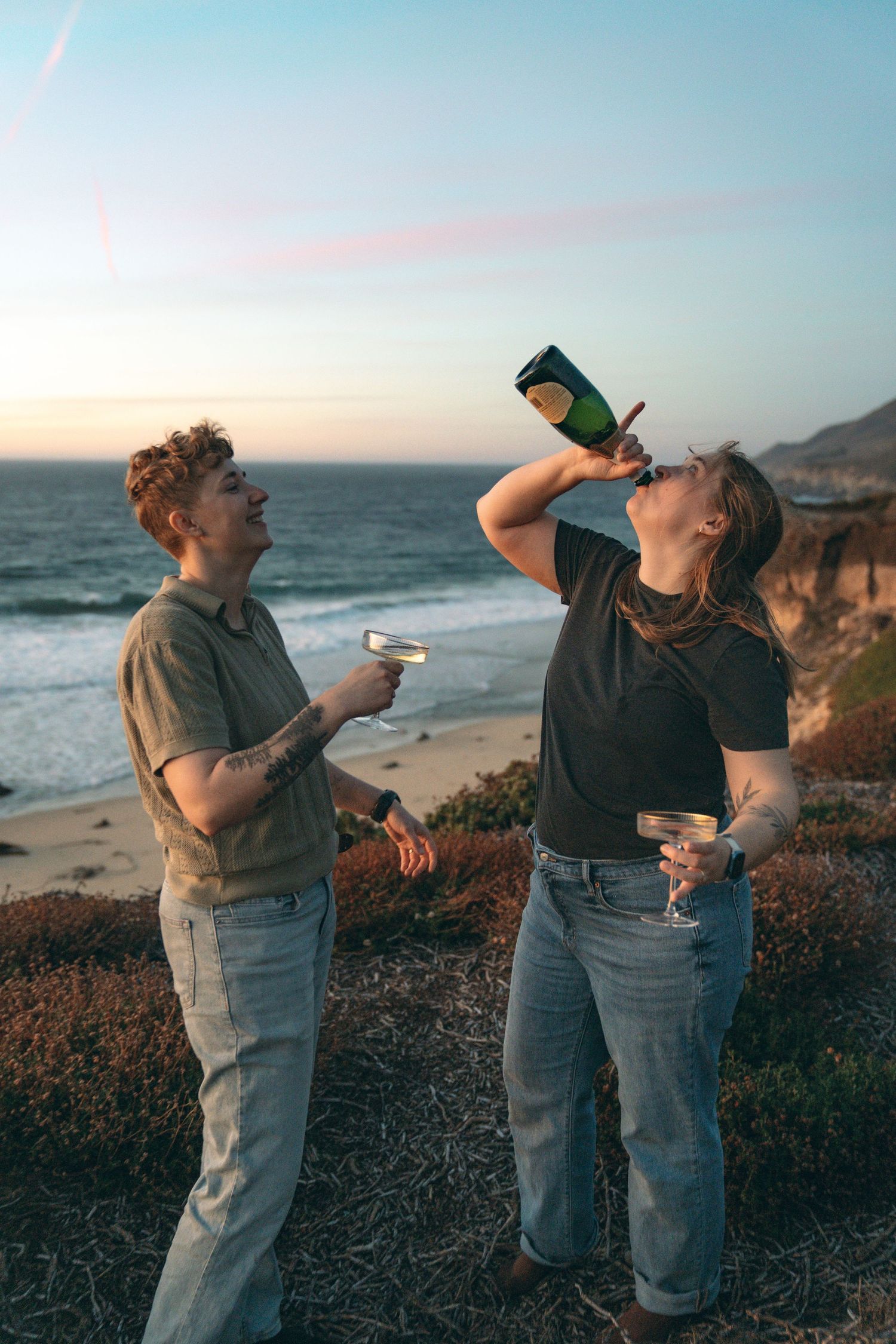 Friends sharing drinks and laughs together on a coastal overlook at dusk.