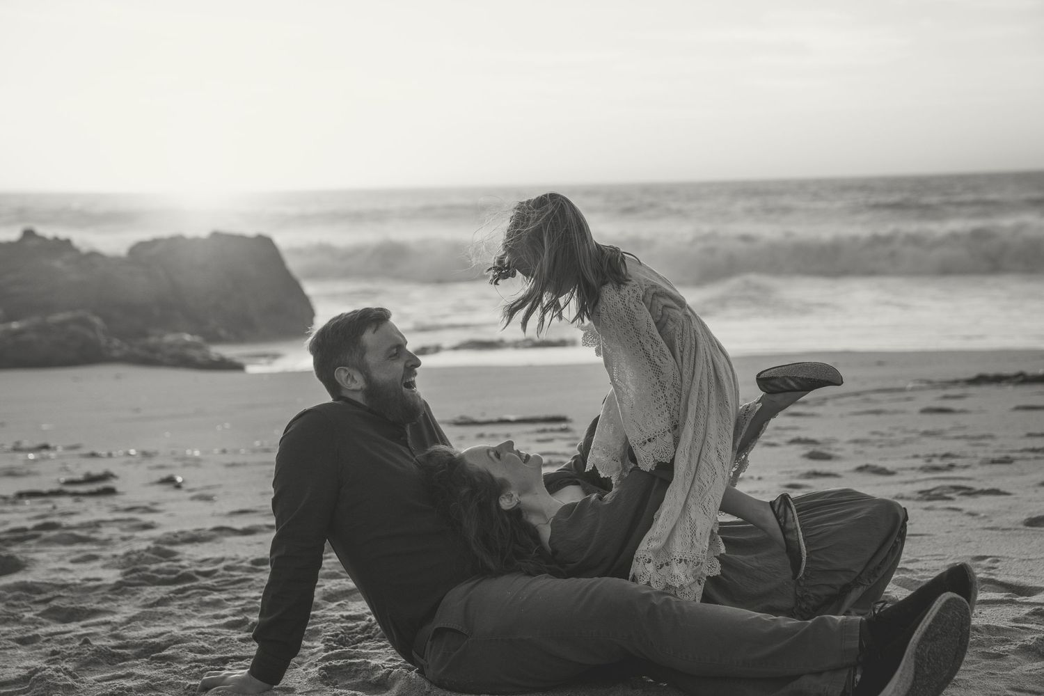 Black and white photo of people enjoying a romantic moment on the beach at sunset with ocean waves visible.