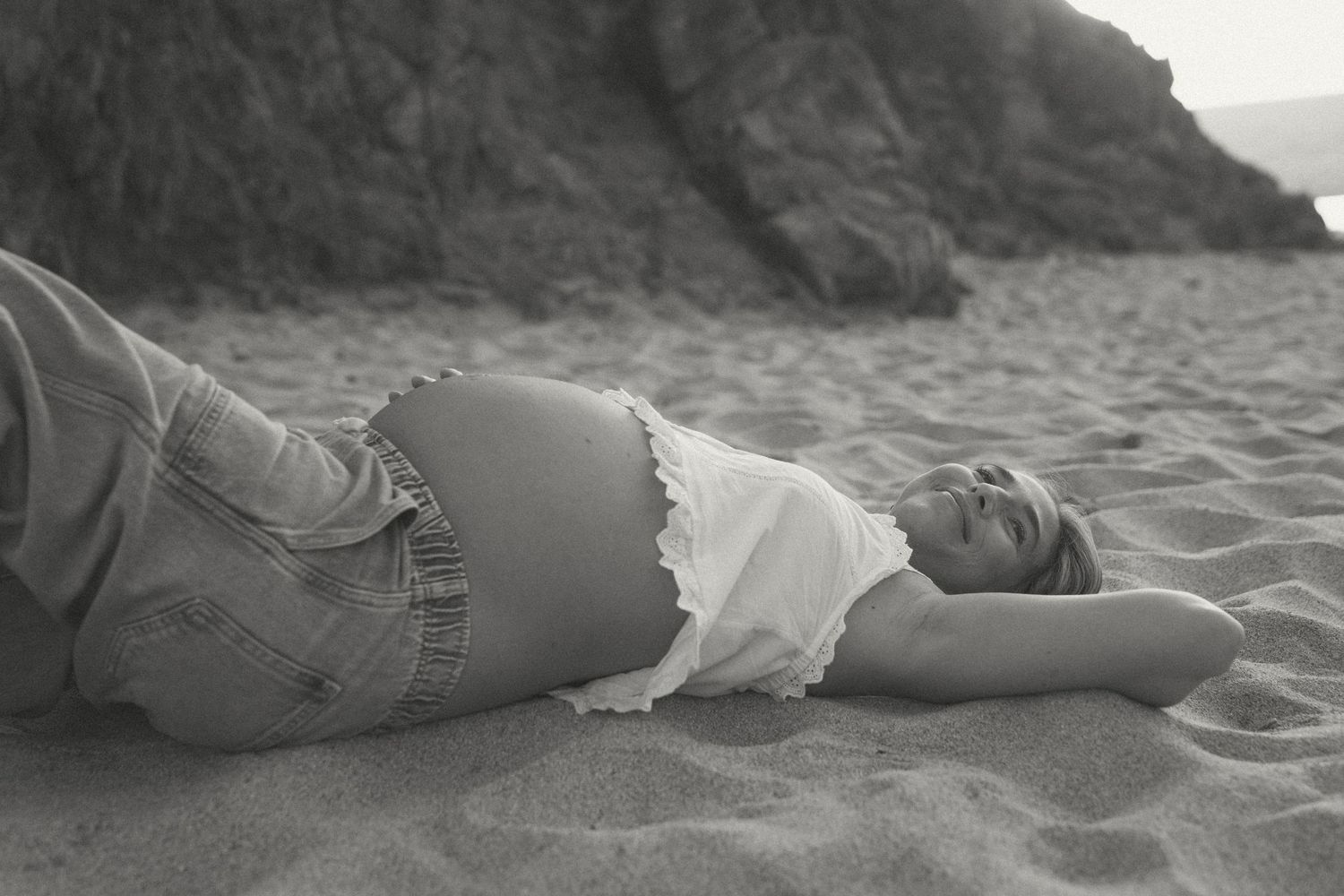 A series of black and white photographs showing someone lying on a sandy beach in various relaxed poses.