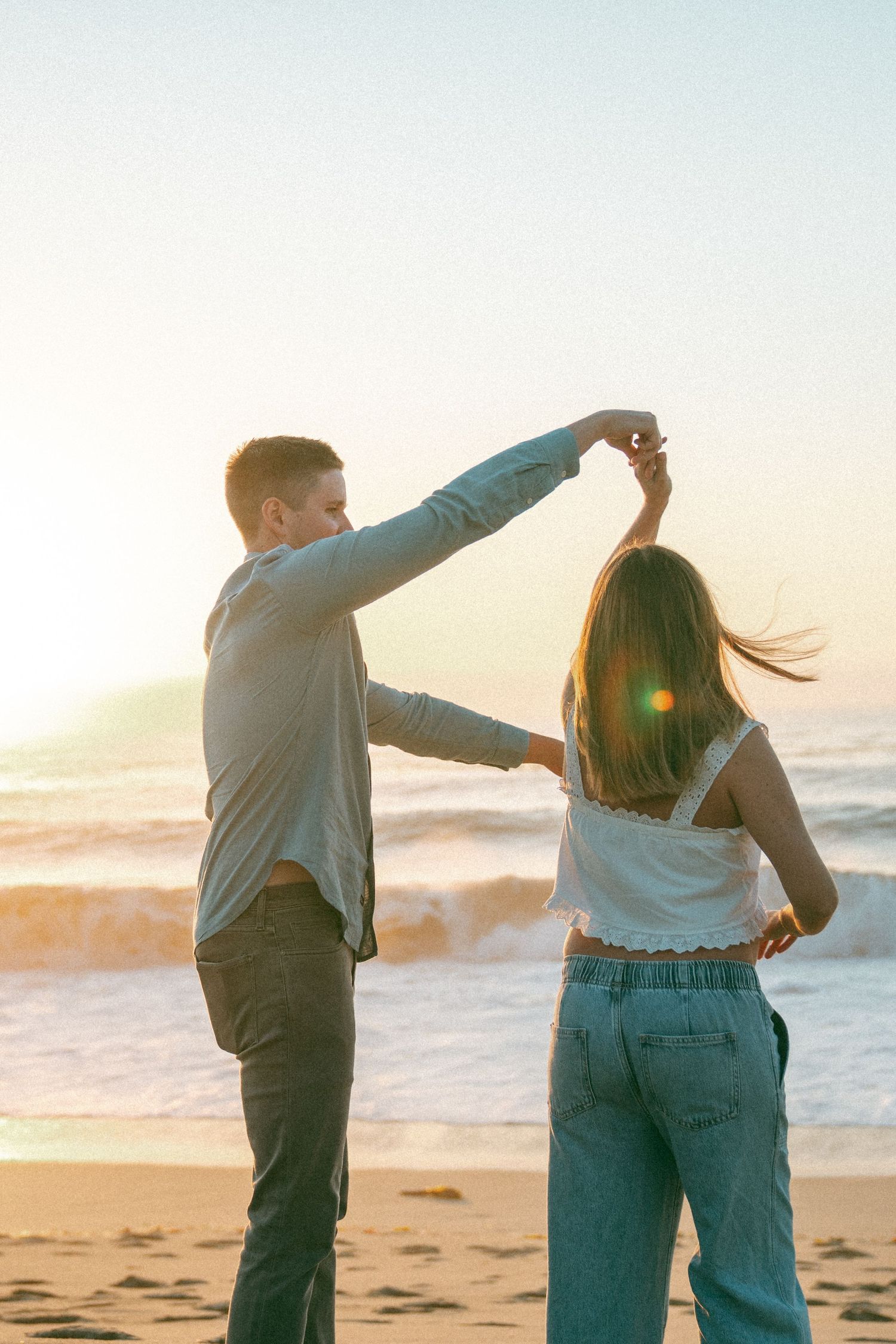 Couple dancing together on a beach at sunset with their backs turned to the camera.