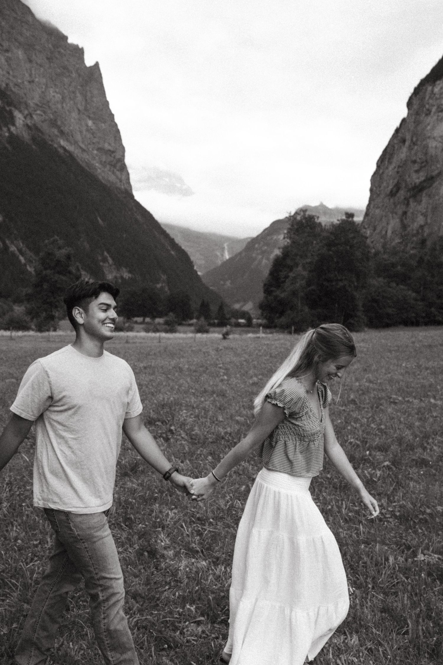Two people hold hands while walking through a stunning mountain valley with dramatic cliffs.