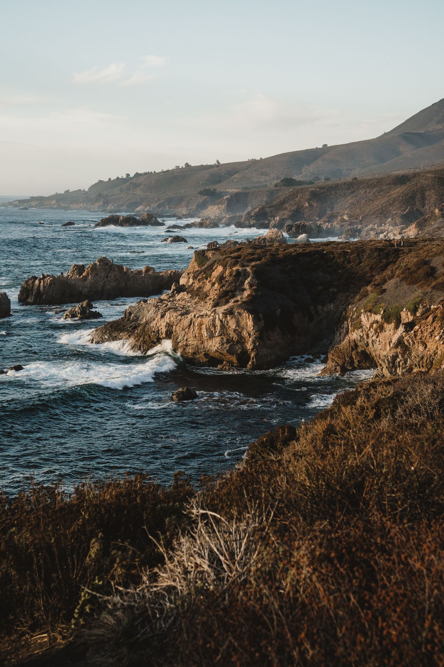 Dramatic coastal cliffs and rocky shoreline of the Big Sur coastline in California during sunset.