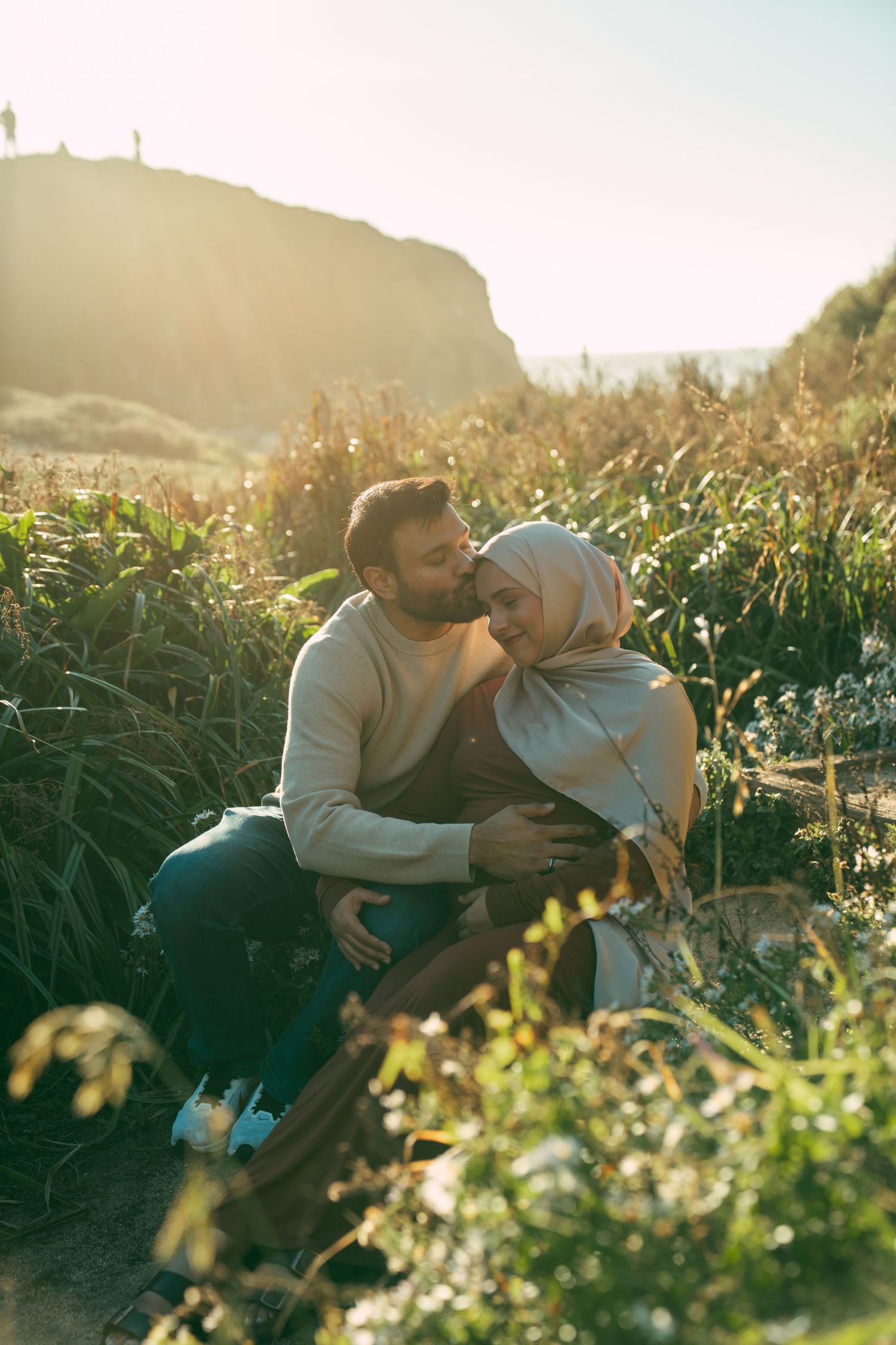 A couple shares an intimate moment together in a sunlit cornfield during golden hour.