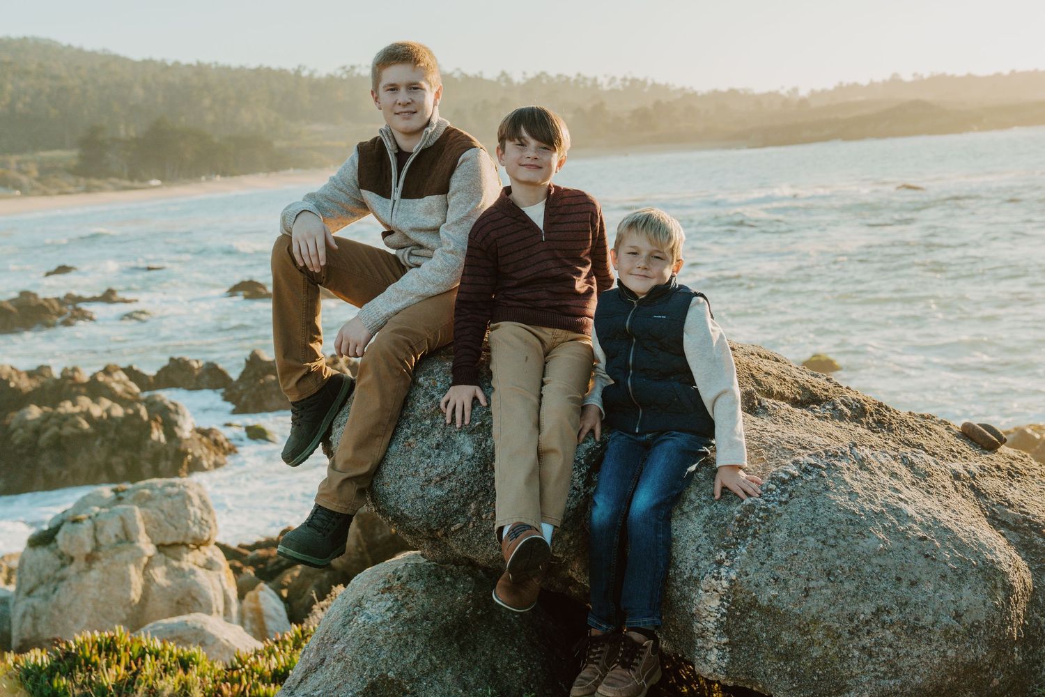 People sitting together on coastal rocks during golden sunset at a scenic beach overlook.