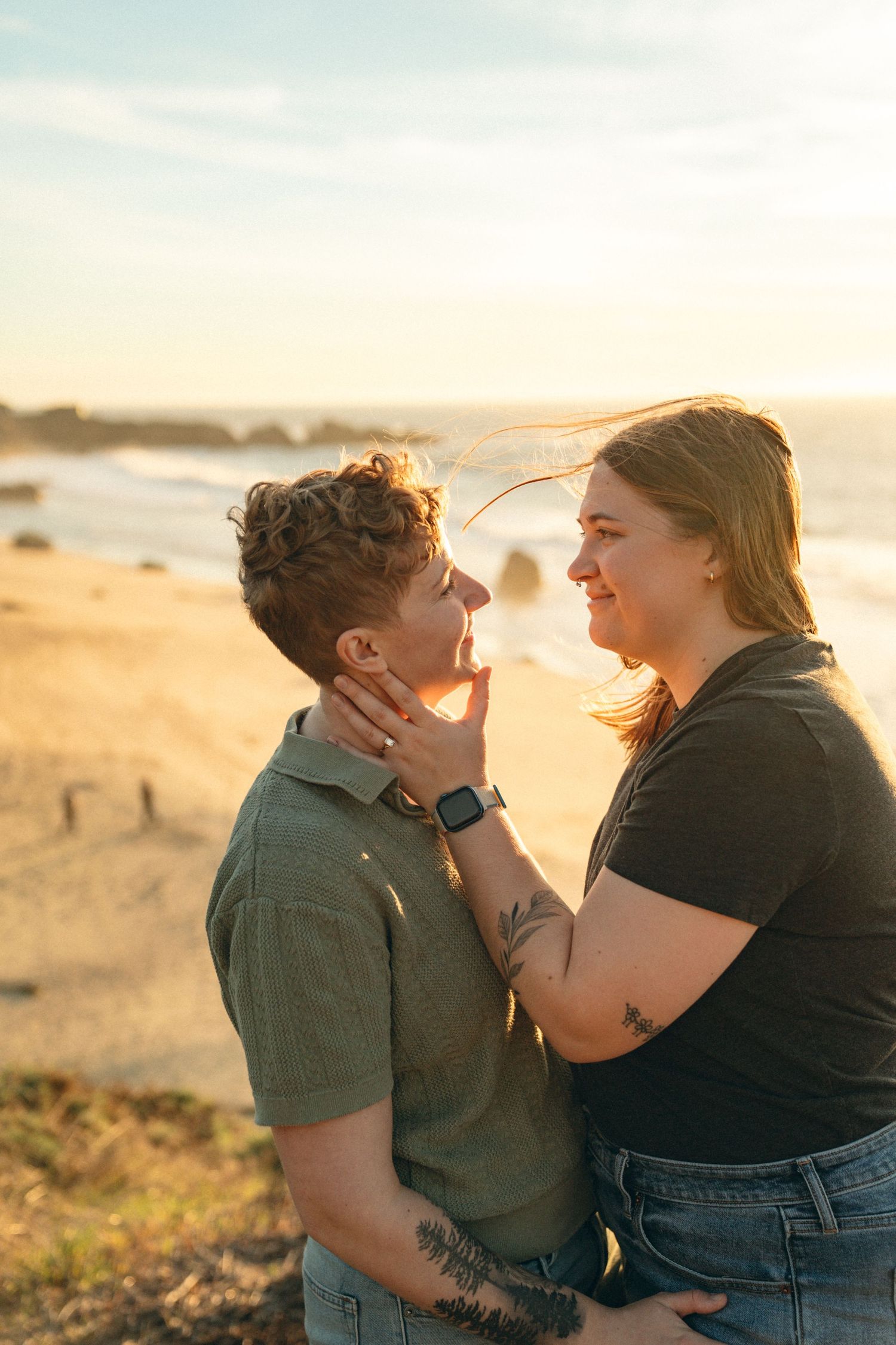 A romantic couple shares an intimate moment at sunset on a coastal beach with ocean waves in the background.