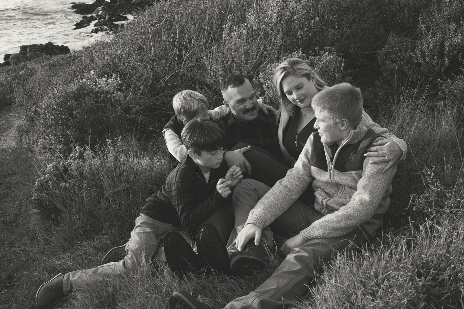 A vintage black and white photograph shows people relaxing together on a grassy hillside outdoors.