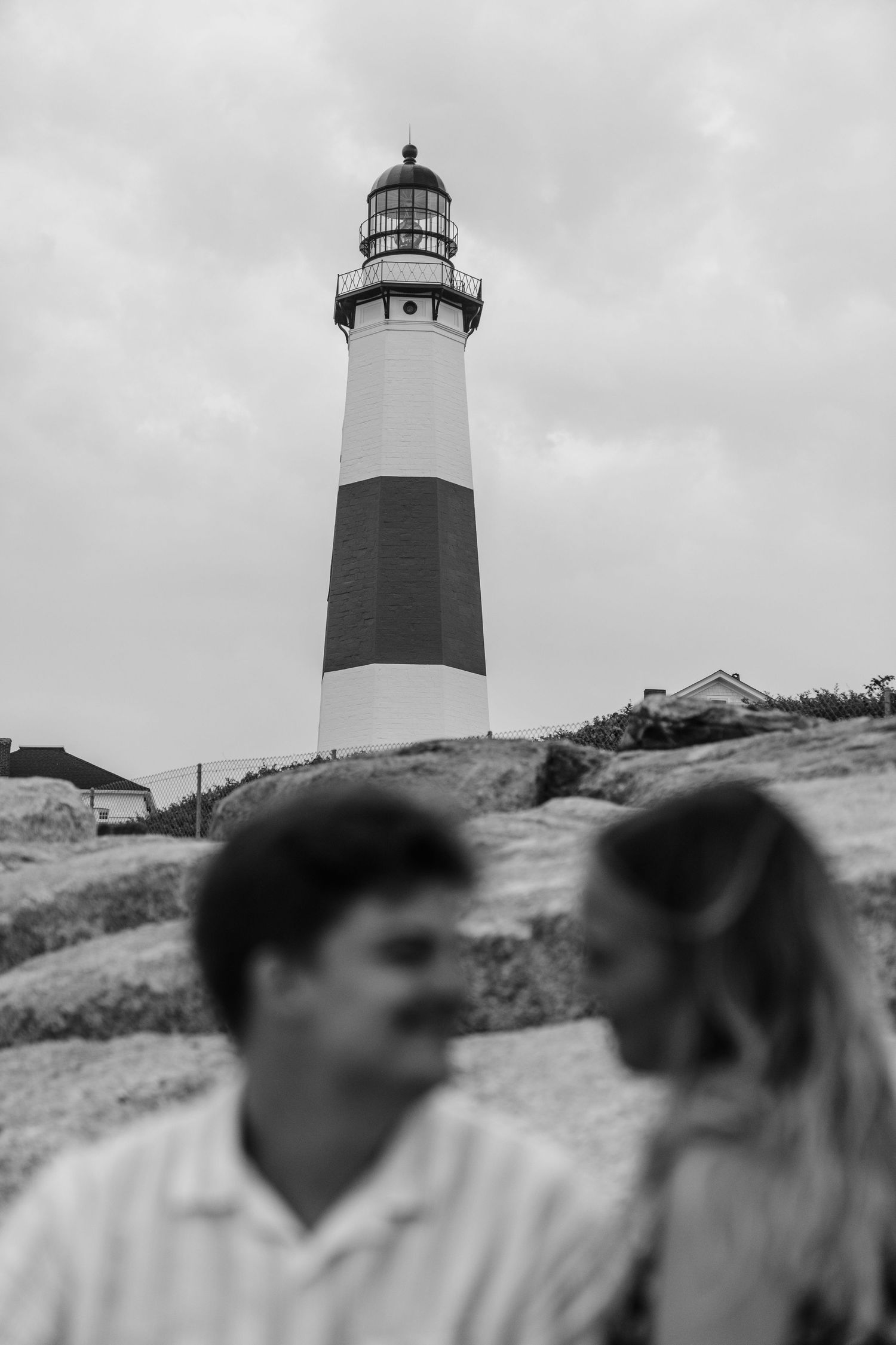 A black and white photo of a lighthouse towering above with a couple in soft focus below.