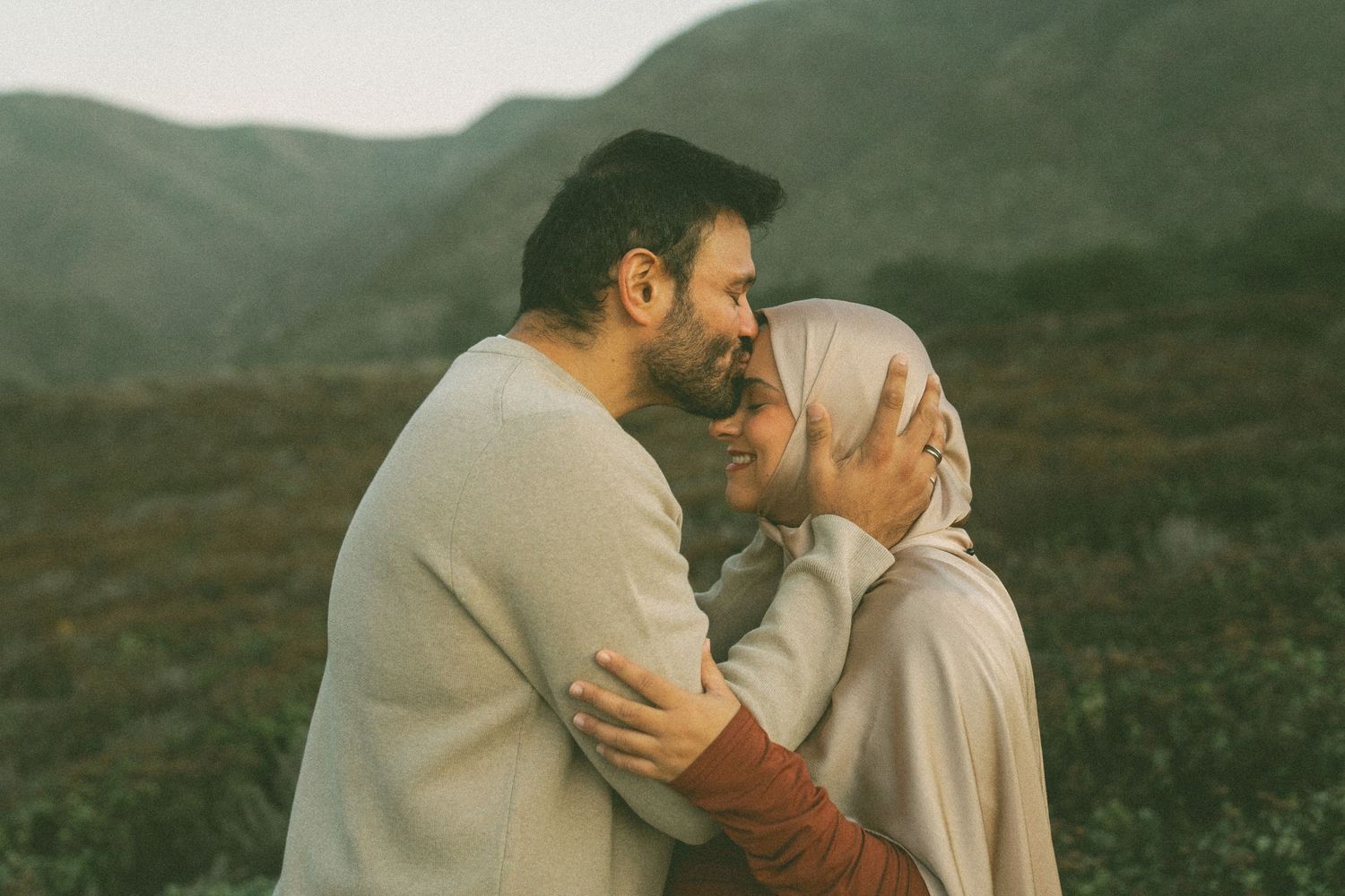 Two people embrace intimately in a romantic moment against a misty mountain landscape backdrop.