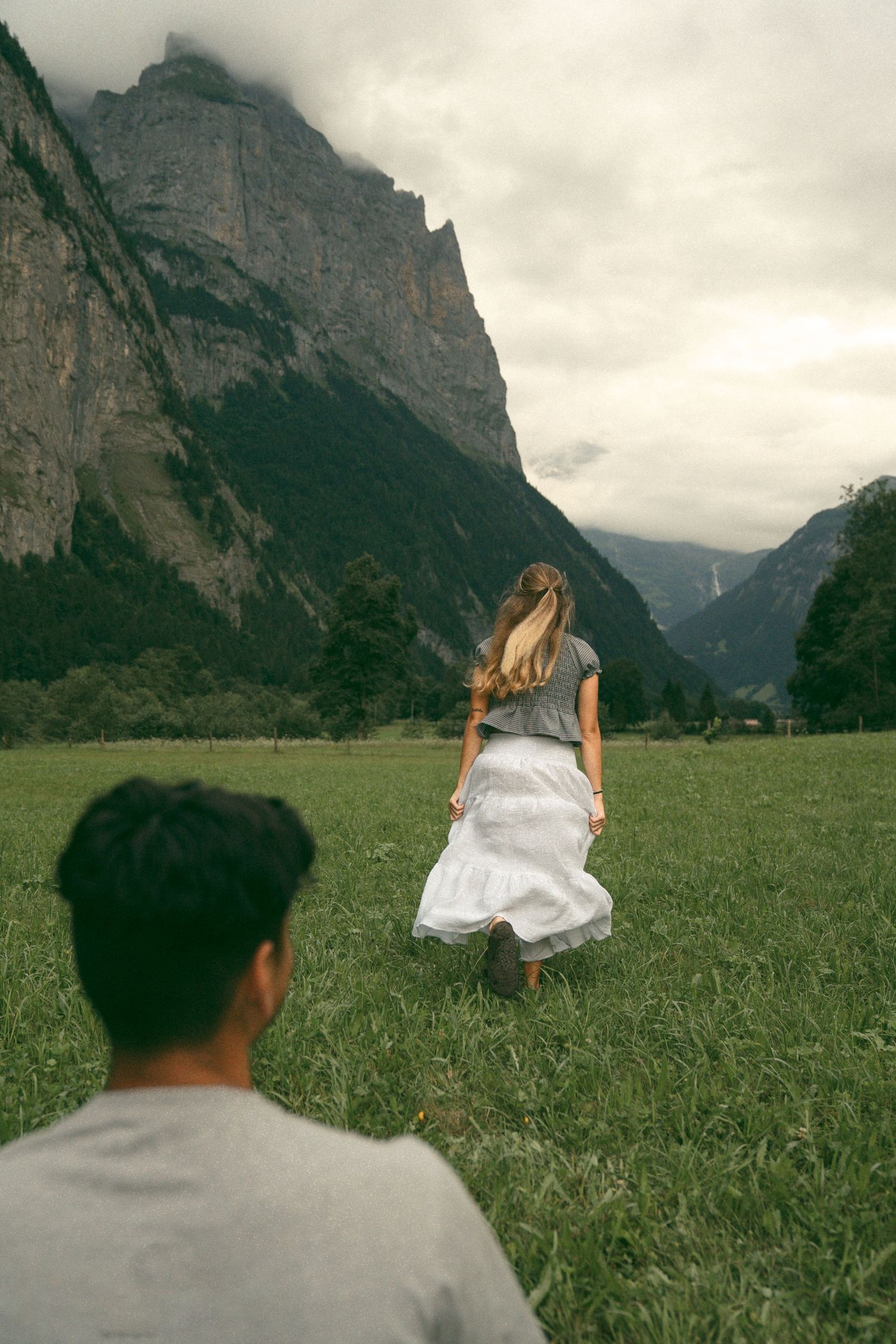 A couple enjoys a picturesque moment in a grassy meadow surrounded by towering mountain peaks in the Alps.