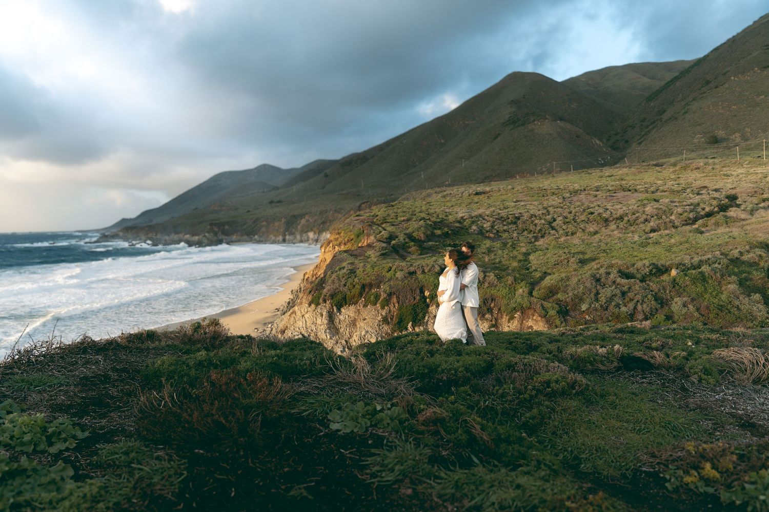 Dramatic panoramic view of Big Sur's rugged coastline with mountains meeting the Pacific Ocean under moody skies.