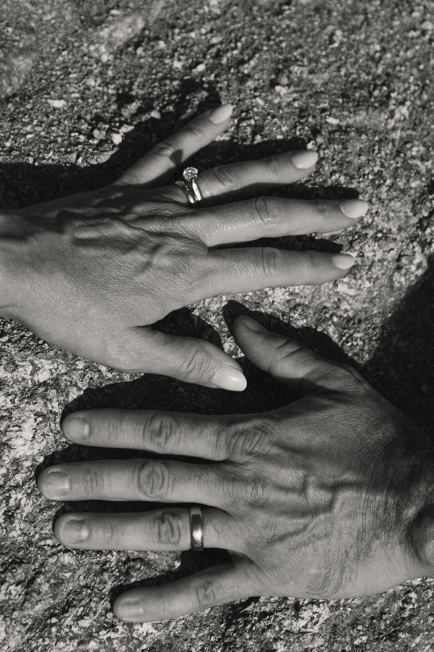 Black and white close-up sequence of two hands reaching towards each other against a textured surface.