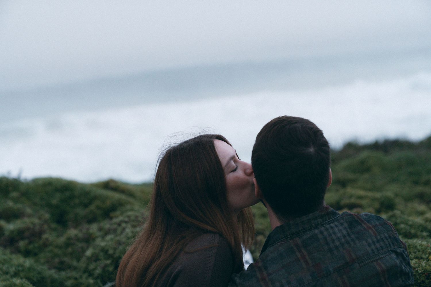Romantic couple embracing on coastal cliffs during moody afternoon.