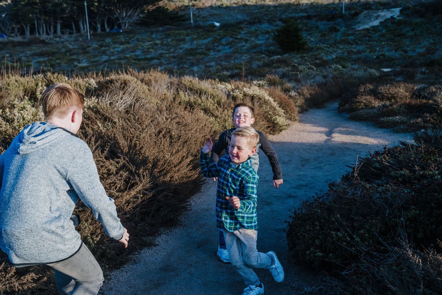A series of family members walking on a winding dirt trail through coastal brush at sunset.