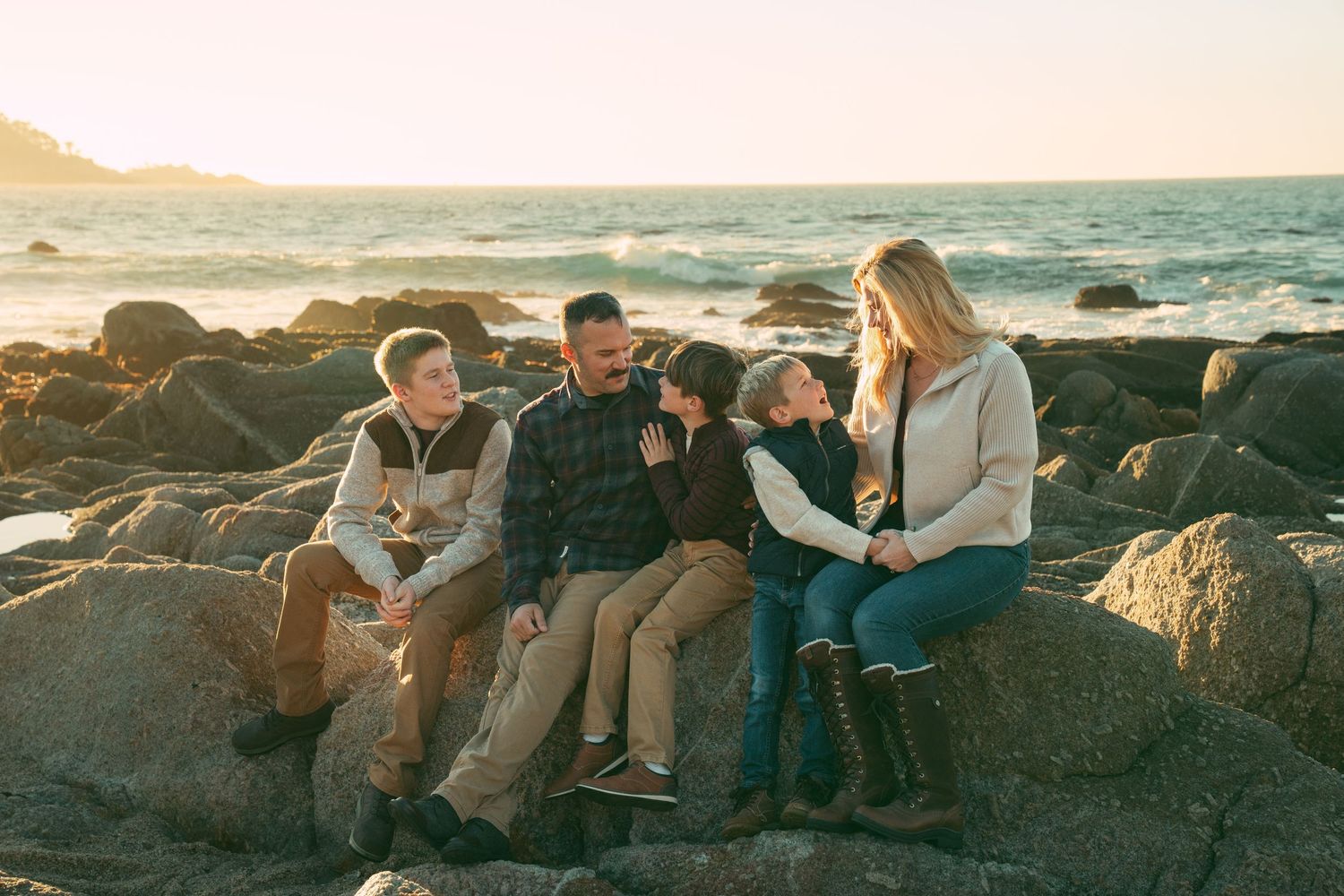 People relaxing on rocky coastal formations at sunset with ocean waves in the background.