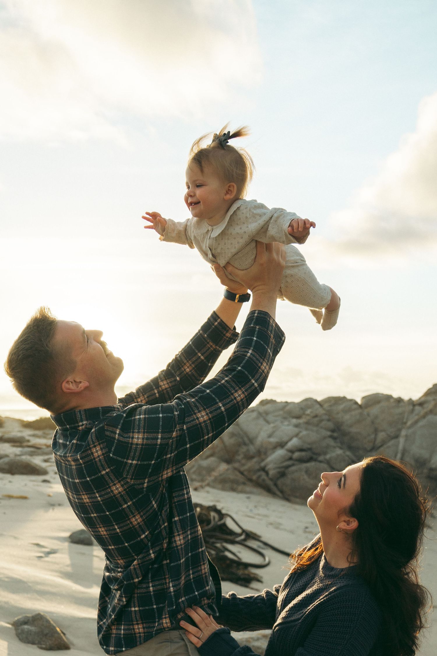A joyful family moment captured on a rocky beach at sunset with playful interactions and laughter.