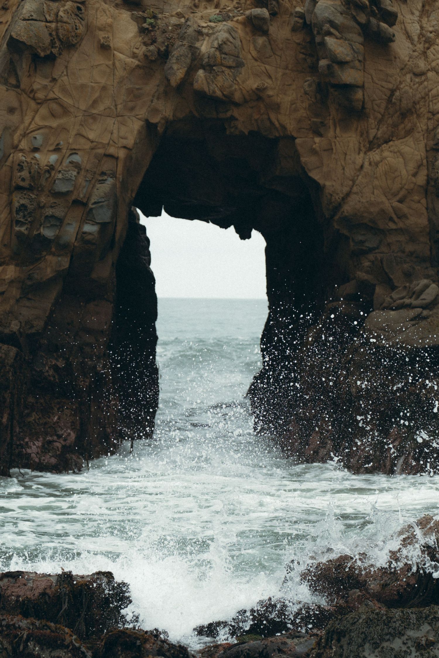 Ocean waves crash through natural rock archways along a rugged coastal cliff formation.