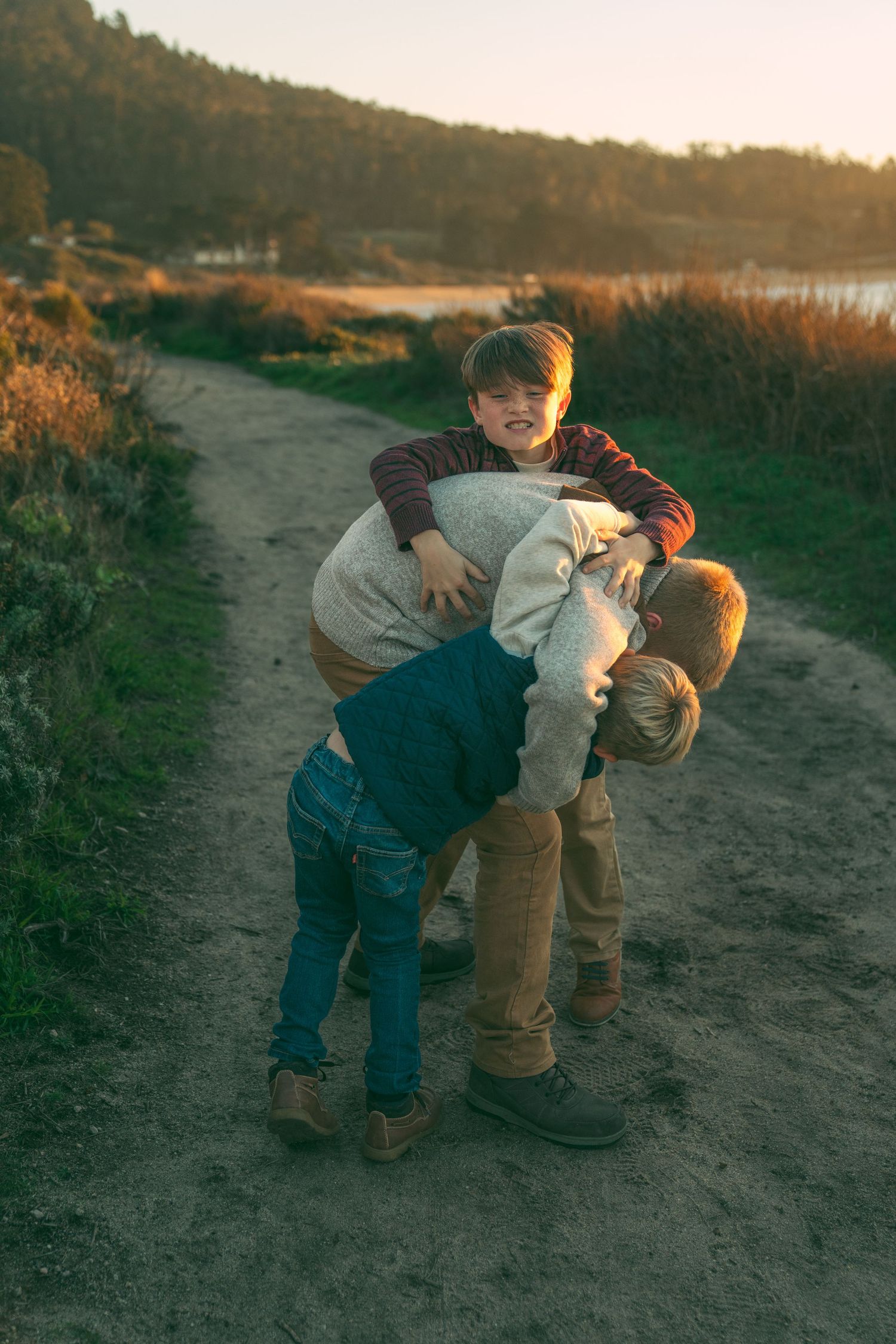 A couple playfully dips and dances on a dirt path at sunset with trees in background.