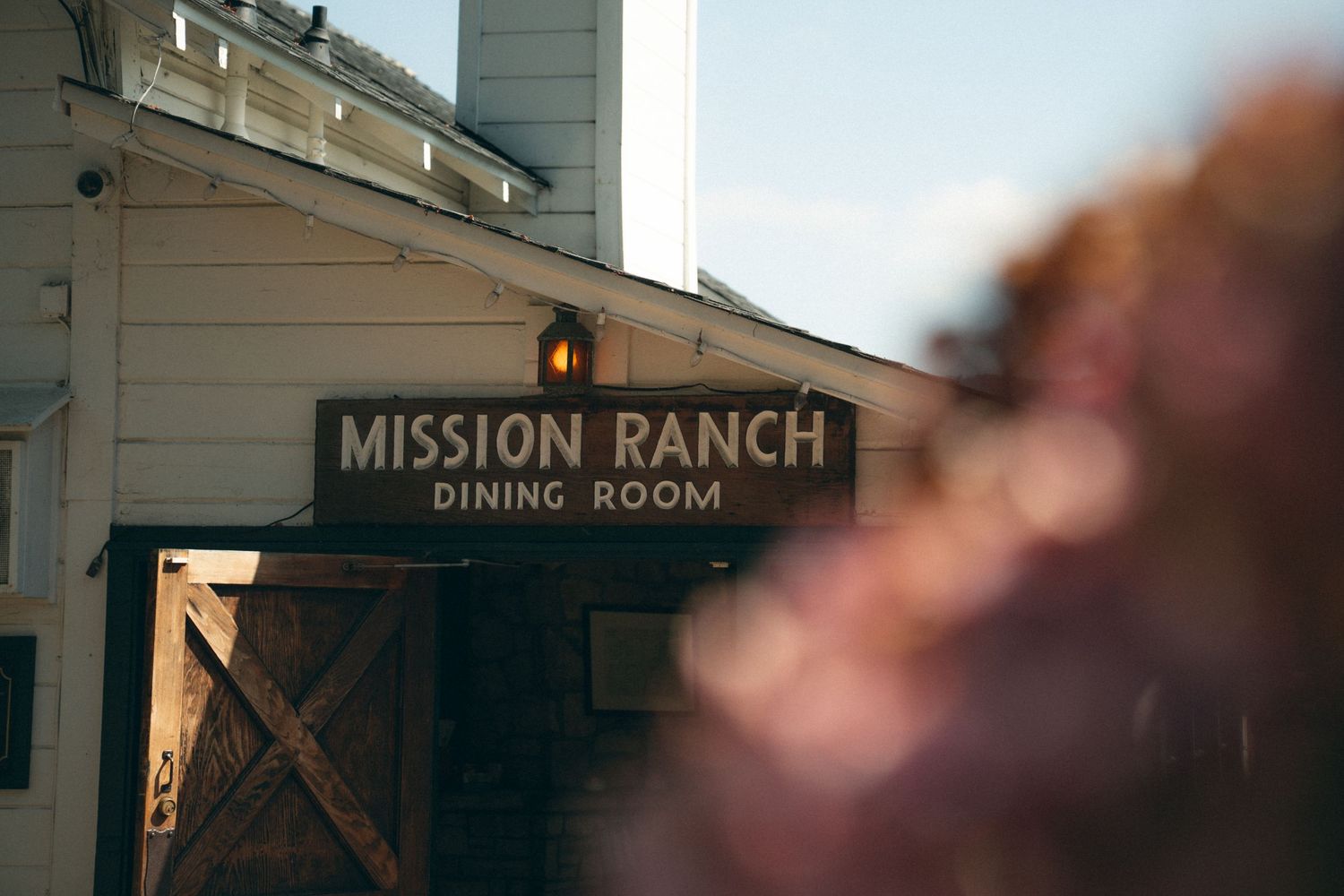 Rustic wooden sign for Mission Ranch displayed on weathered building exterior.