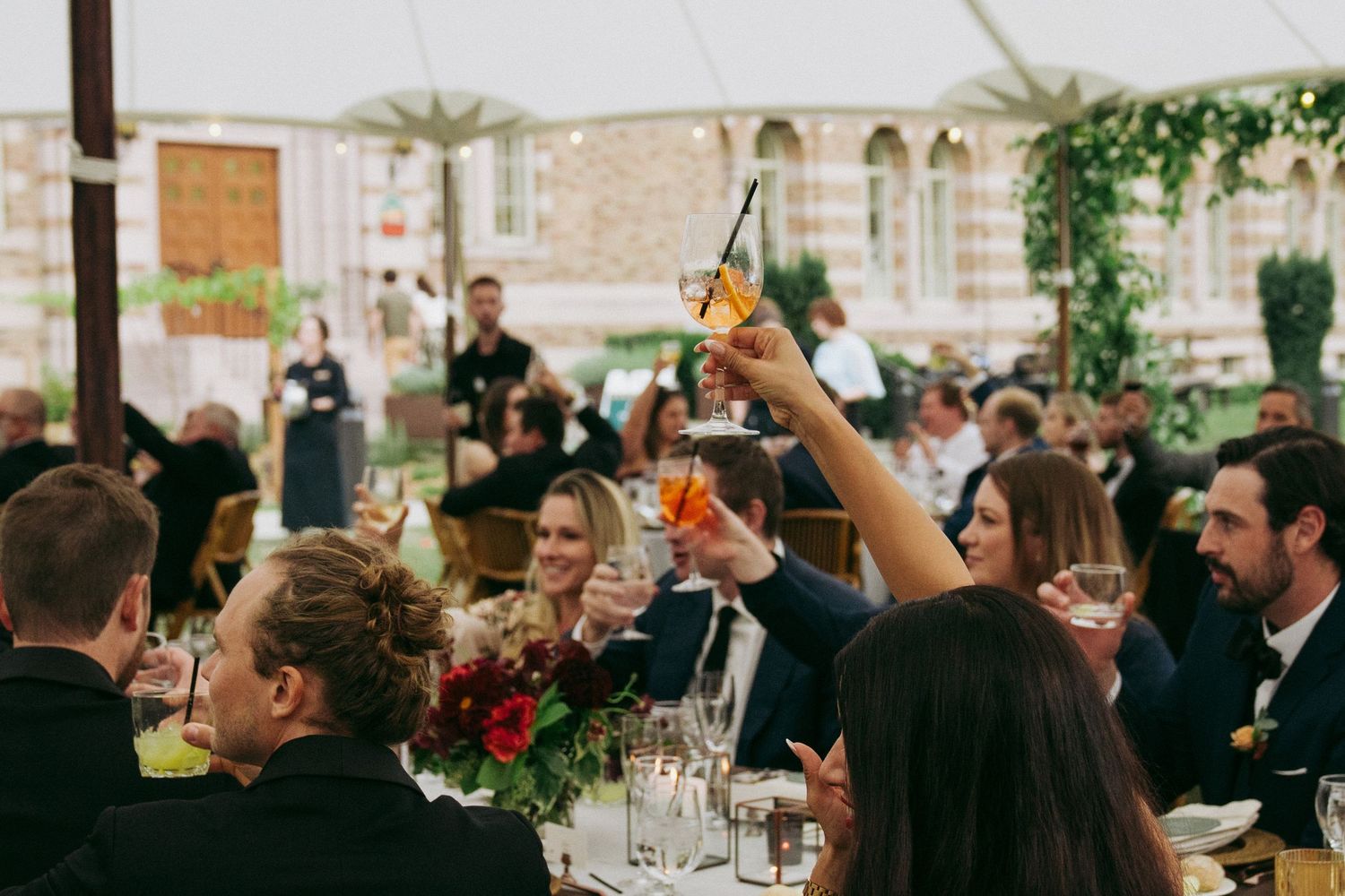 Wedding reception guests raise their glasses in celebration during a toast at an elegant indoor venue.