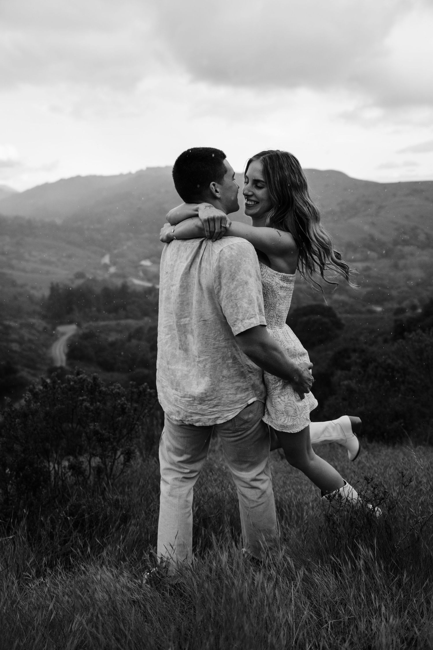 A couple shares an intimate moment in a misty mountain field.