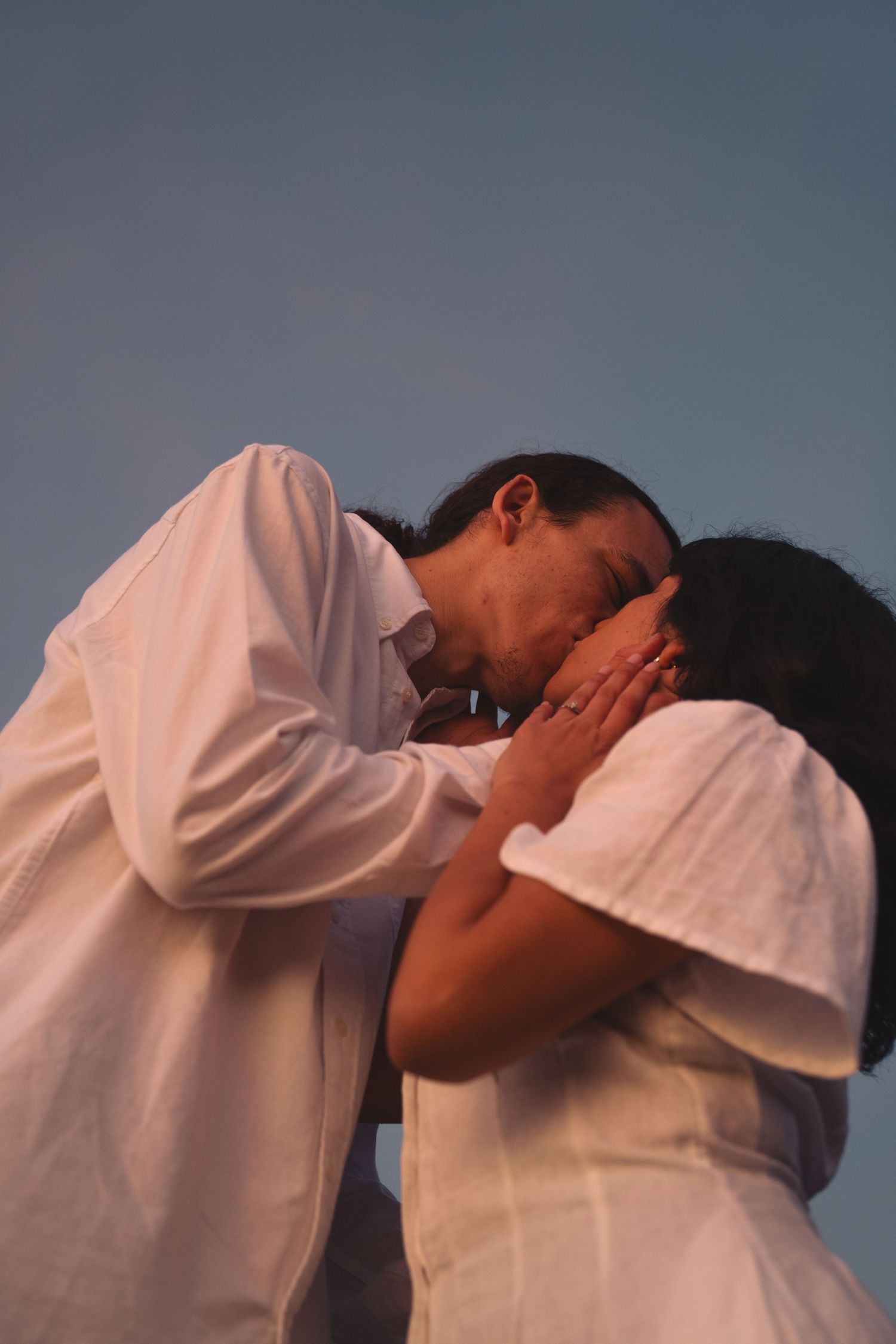 Two people in white clothing share an intimate moment against a dusky blue background.