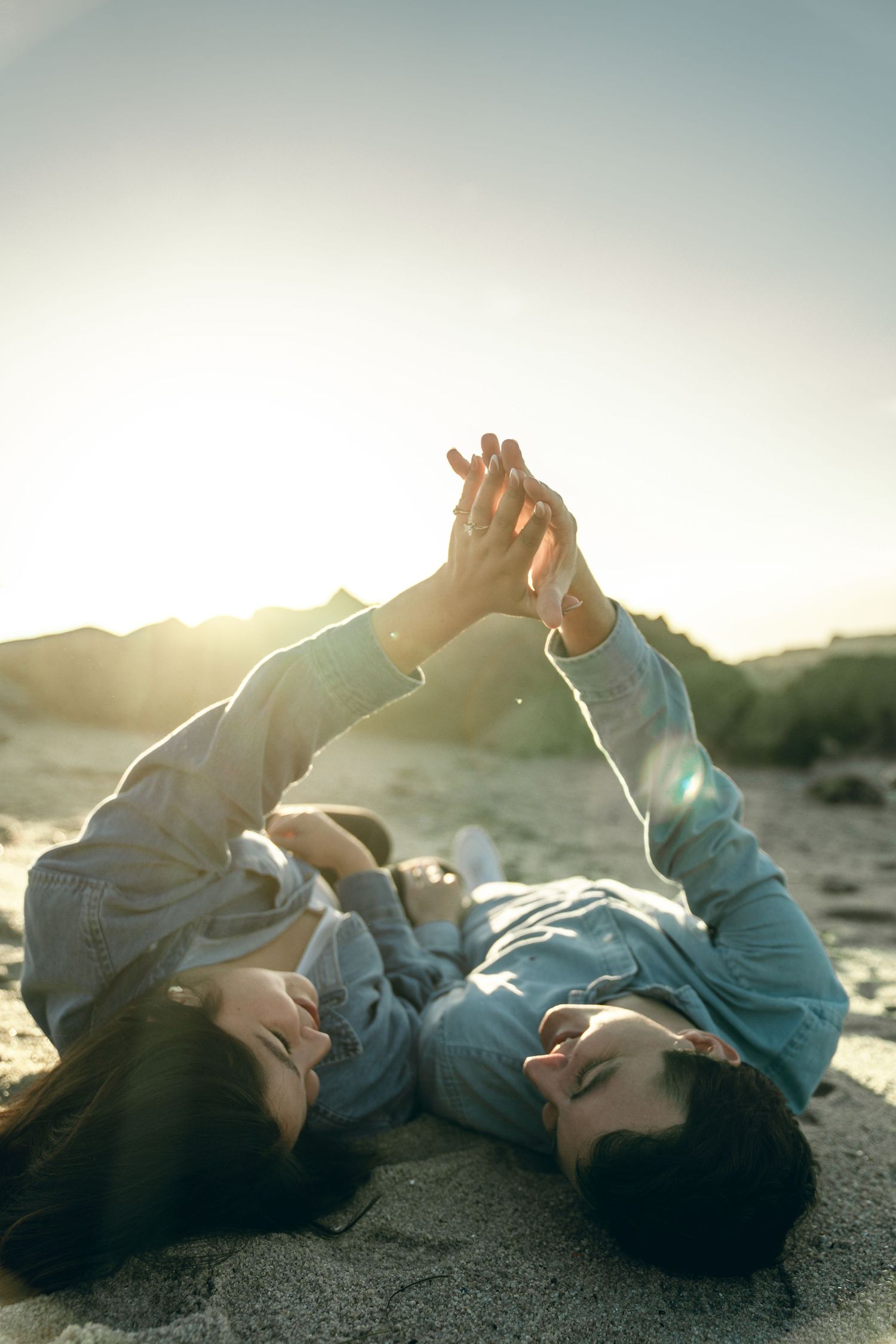 Two people lying on sandy beach sharing tender moments during golden hour.