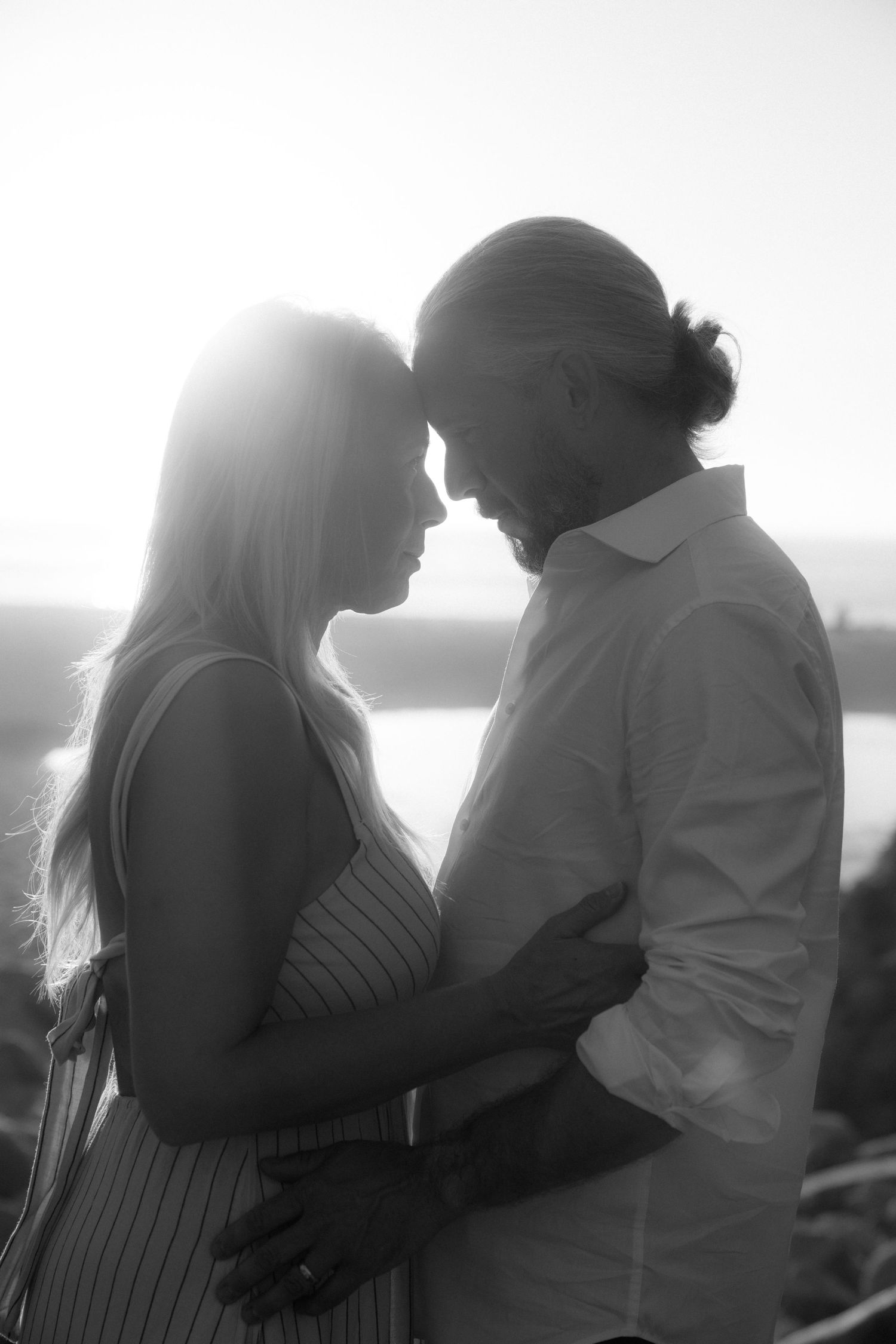 A romantic black and white silhouette of a couple embracing by a lake at sunset, creating an intimate moment.