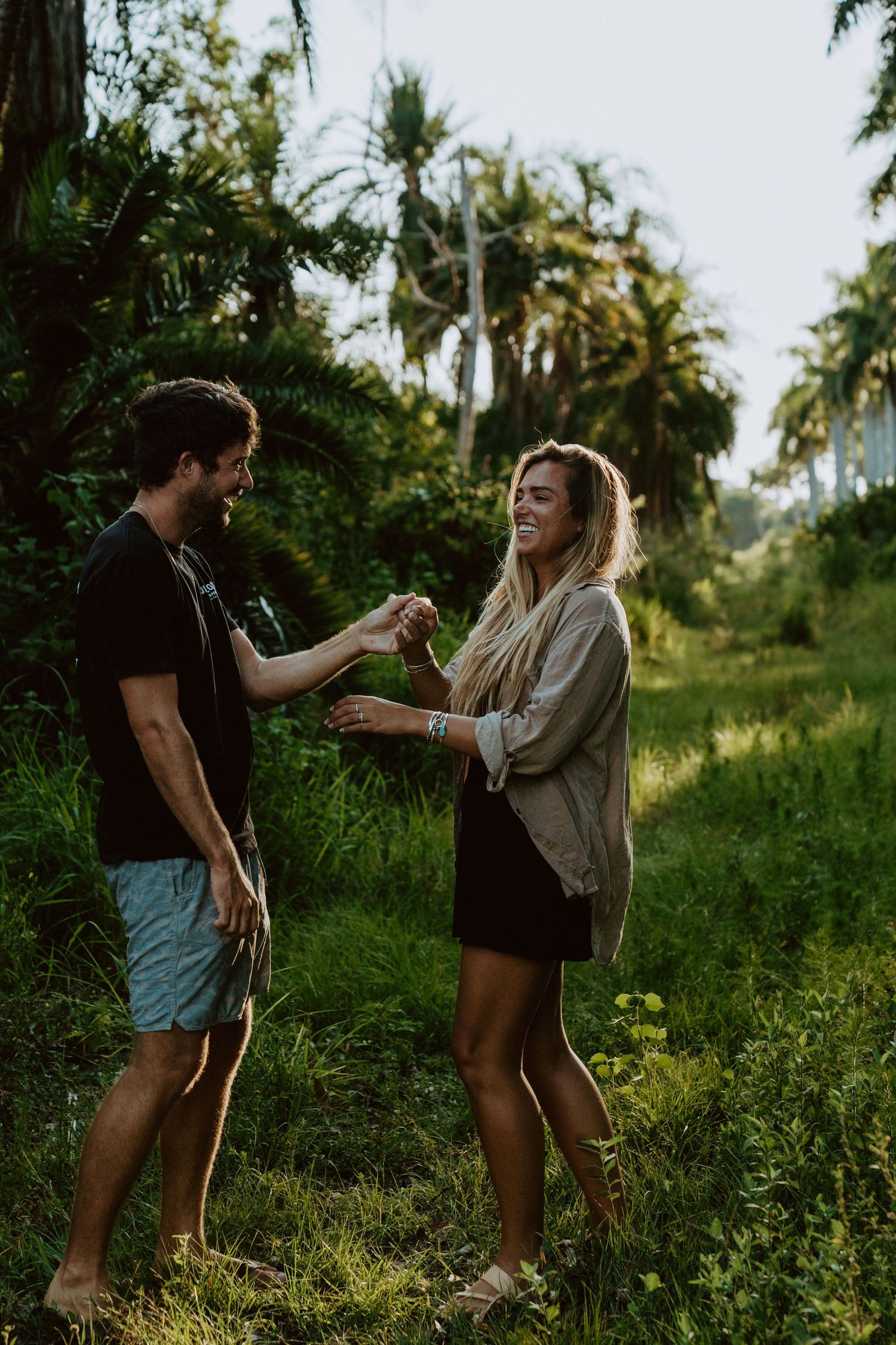 A couple shares a joyful moment together in a lush tropical setting with palm trees during golden hour.
