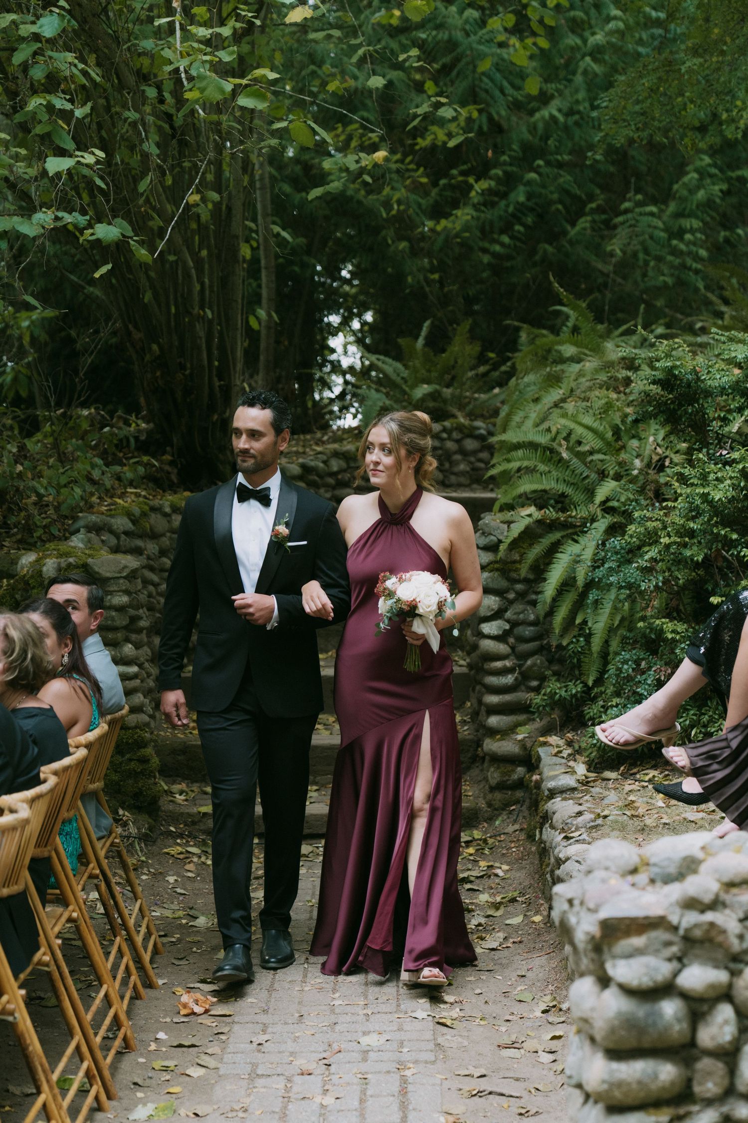 Wedding processional with couples walking down stone-lined garden path.