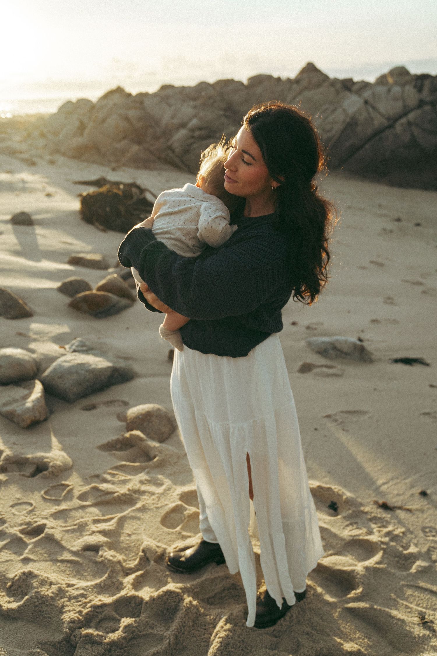 Intimate moments captured on sandy beach with rocky coastline at sunset.