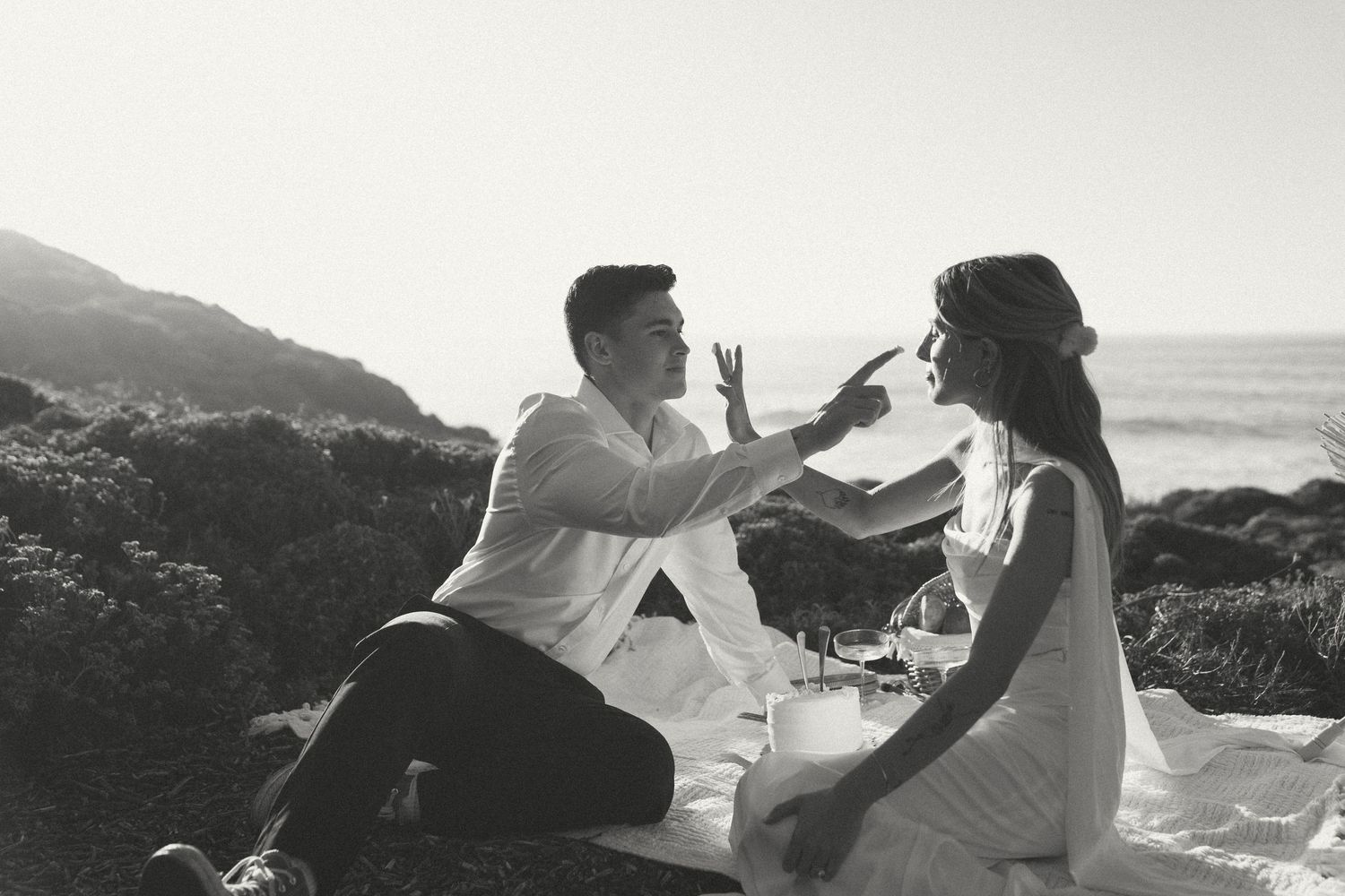 A black and white photo montage shows a romantic couple embracing on a scenic coastal cliff overlooking the ocean.