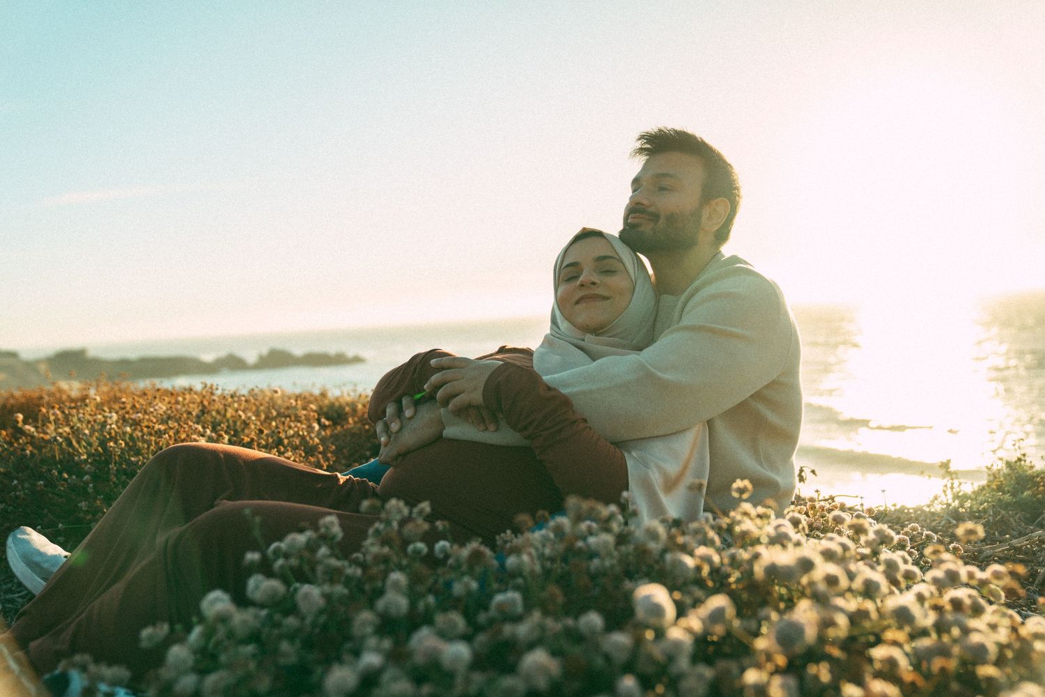 A couple sits together on coastal rocks enjoying a romantic sunset by the ocean.