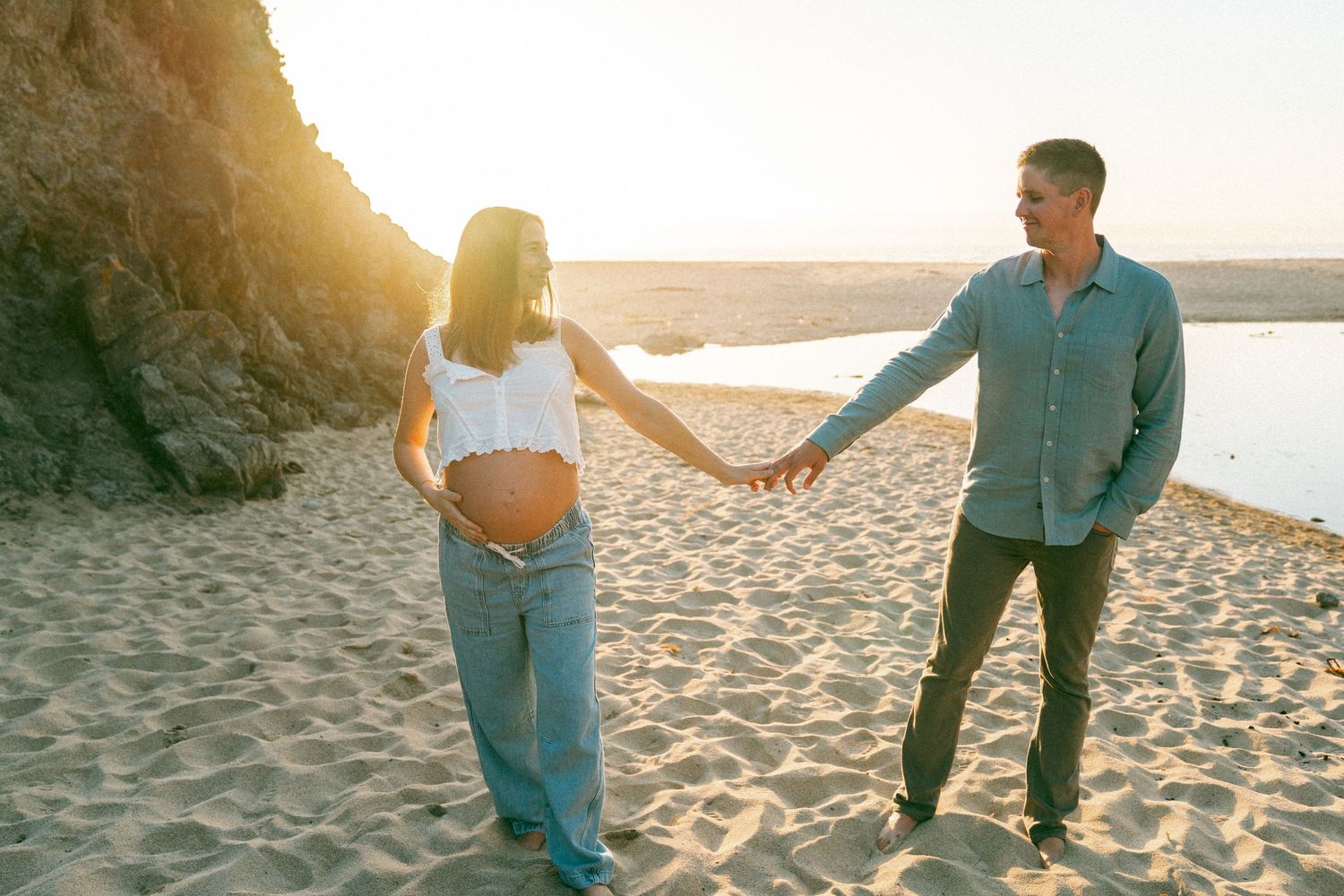 Couple walking hand in hand along a sandy beach at sunset creating romantic silhouettes against the golden sky.