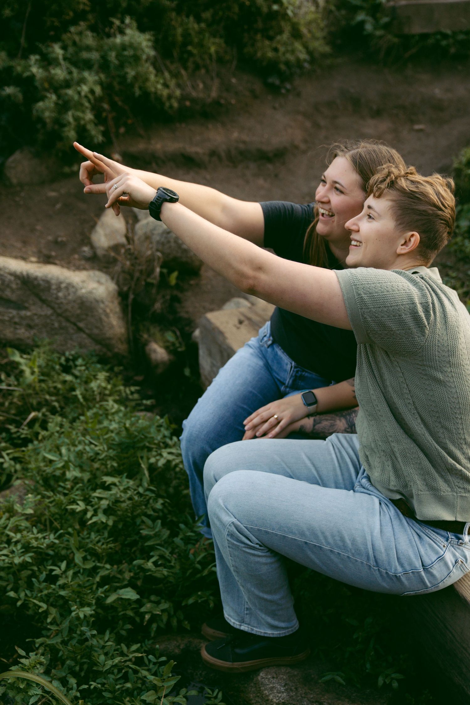 People point and gesture excitedly while sitting among foliage on a coastal hillside.