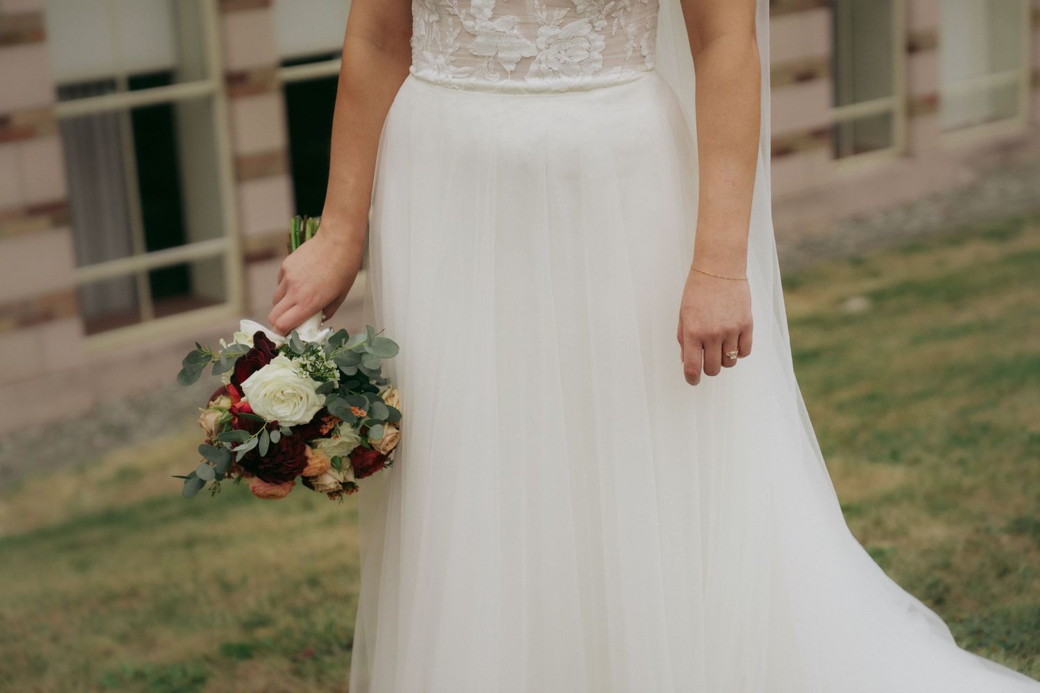 A wedding dress detail showing delicate lace and beadwork on white fabric with a soft, ethereal quality.
