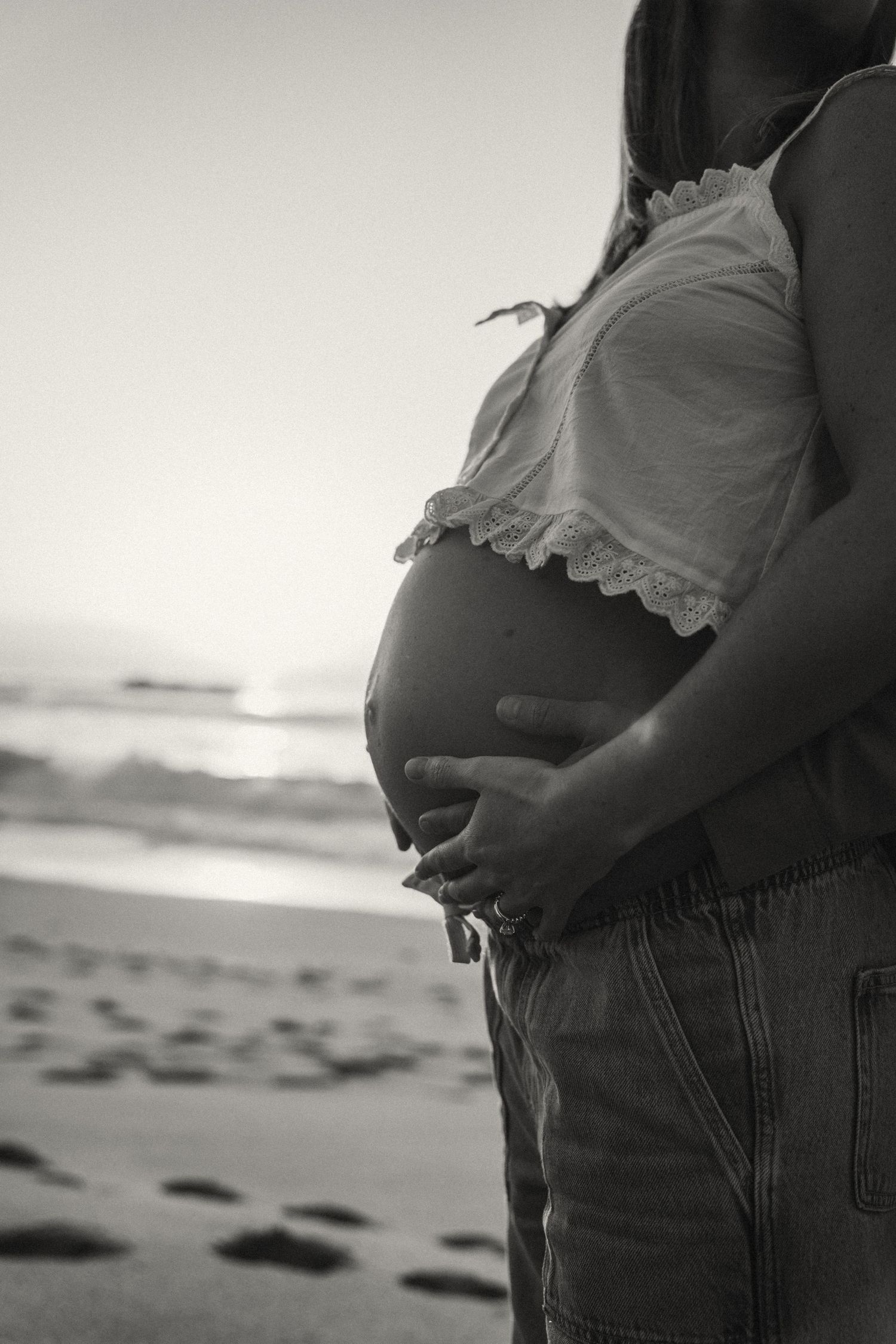 Black and white maternity photo series showing pregnant silhouette against beach background.