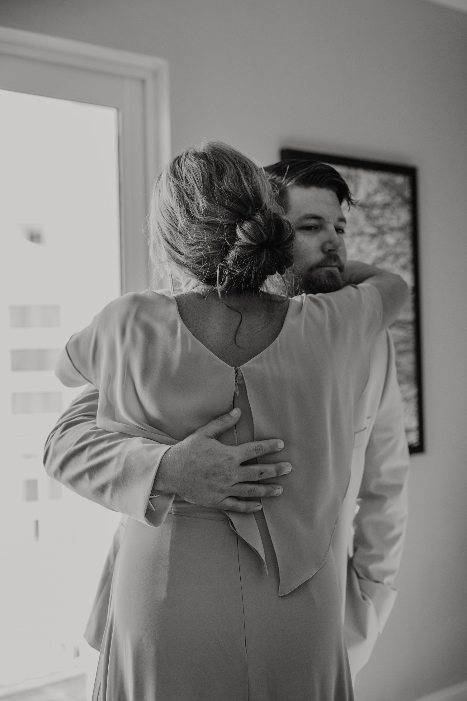 Two people in white formal wear embrace in black and white photos showing a romantic wedding moment.