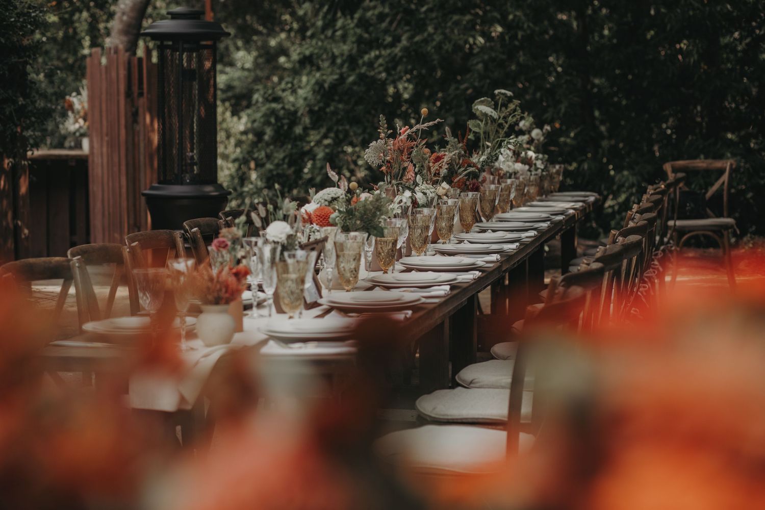 A rustic outdoor wedding reception venue with wooden tables and string lights creating an elegant garden atmosphere.