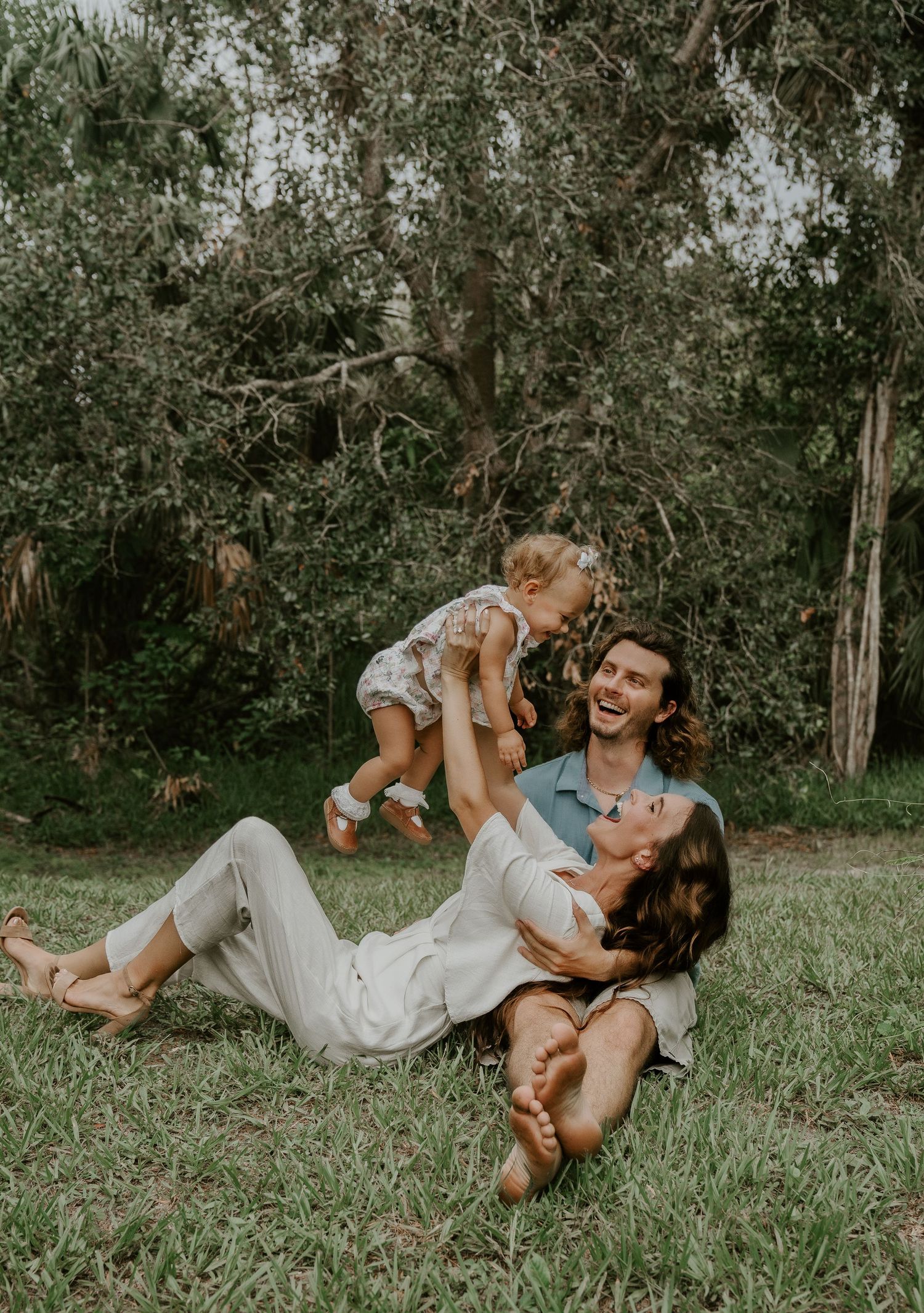 A joyful family moment playing and laughing together on grass under trees.