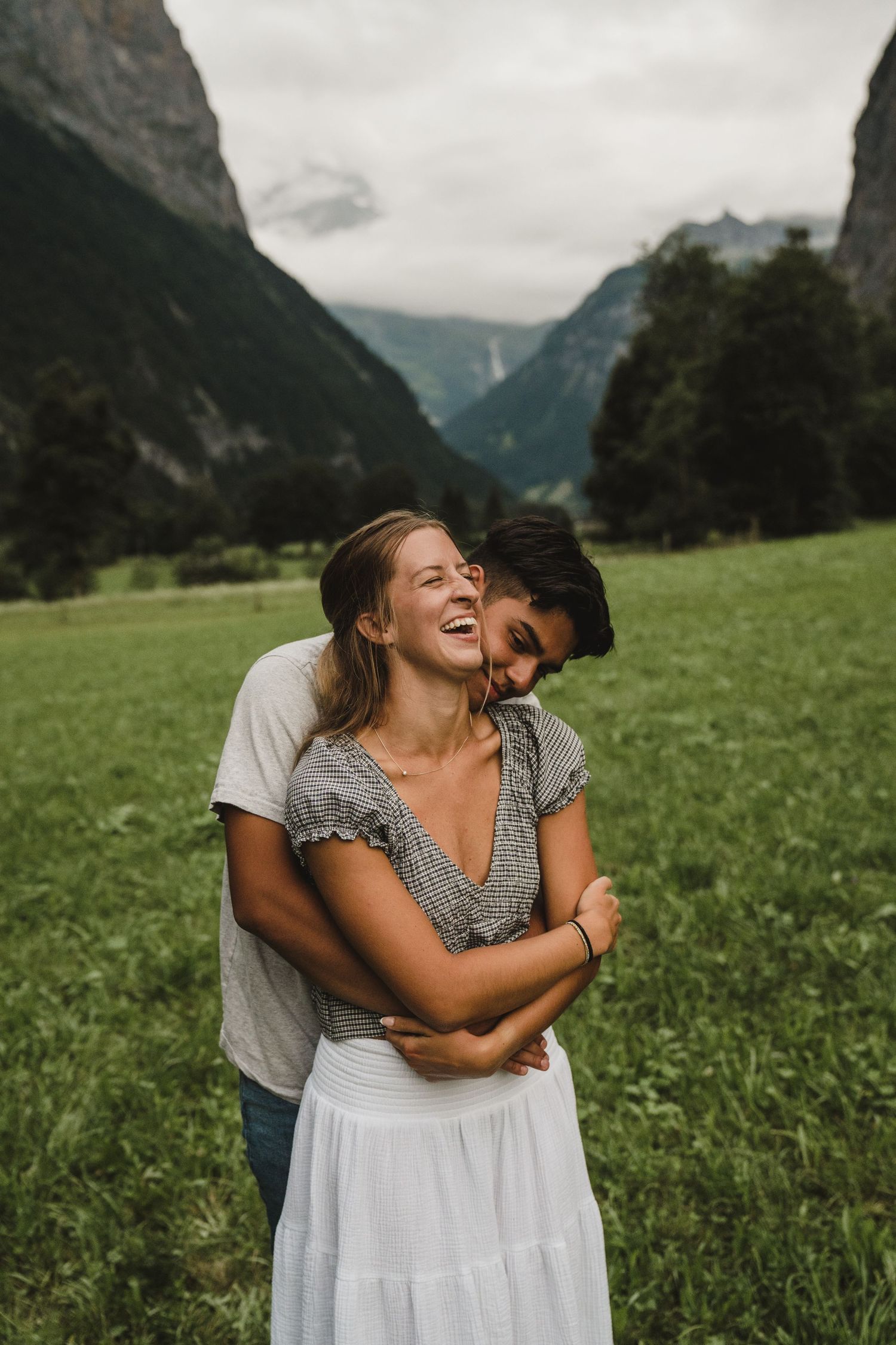 A joyful embrace between two people in a scenic Alpine valley with majestic mountains in the background.