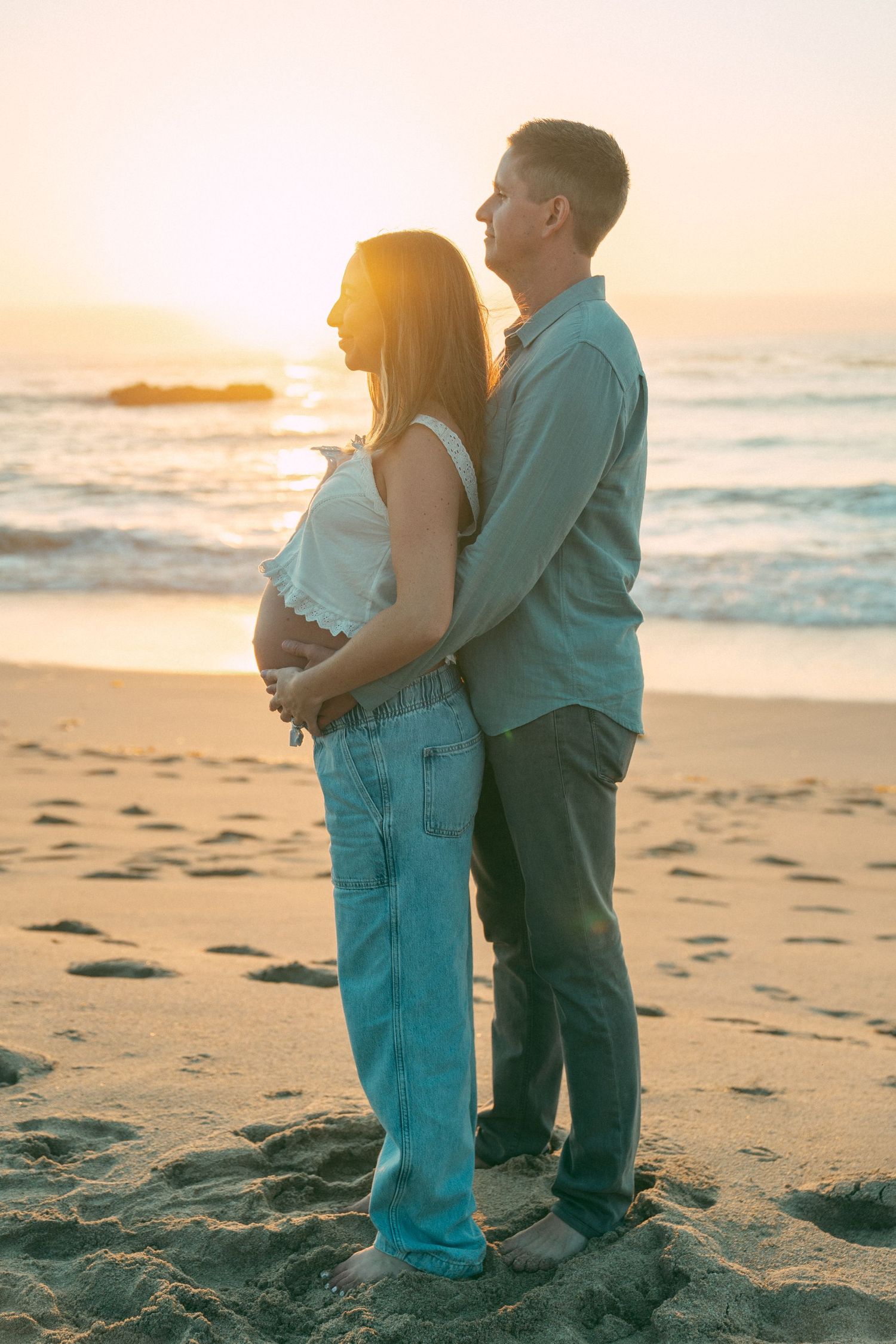 Couple embracing on a sandy beach at sunset with ocean waves in the background.